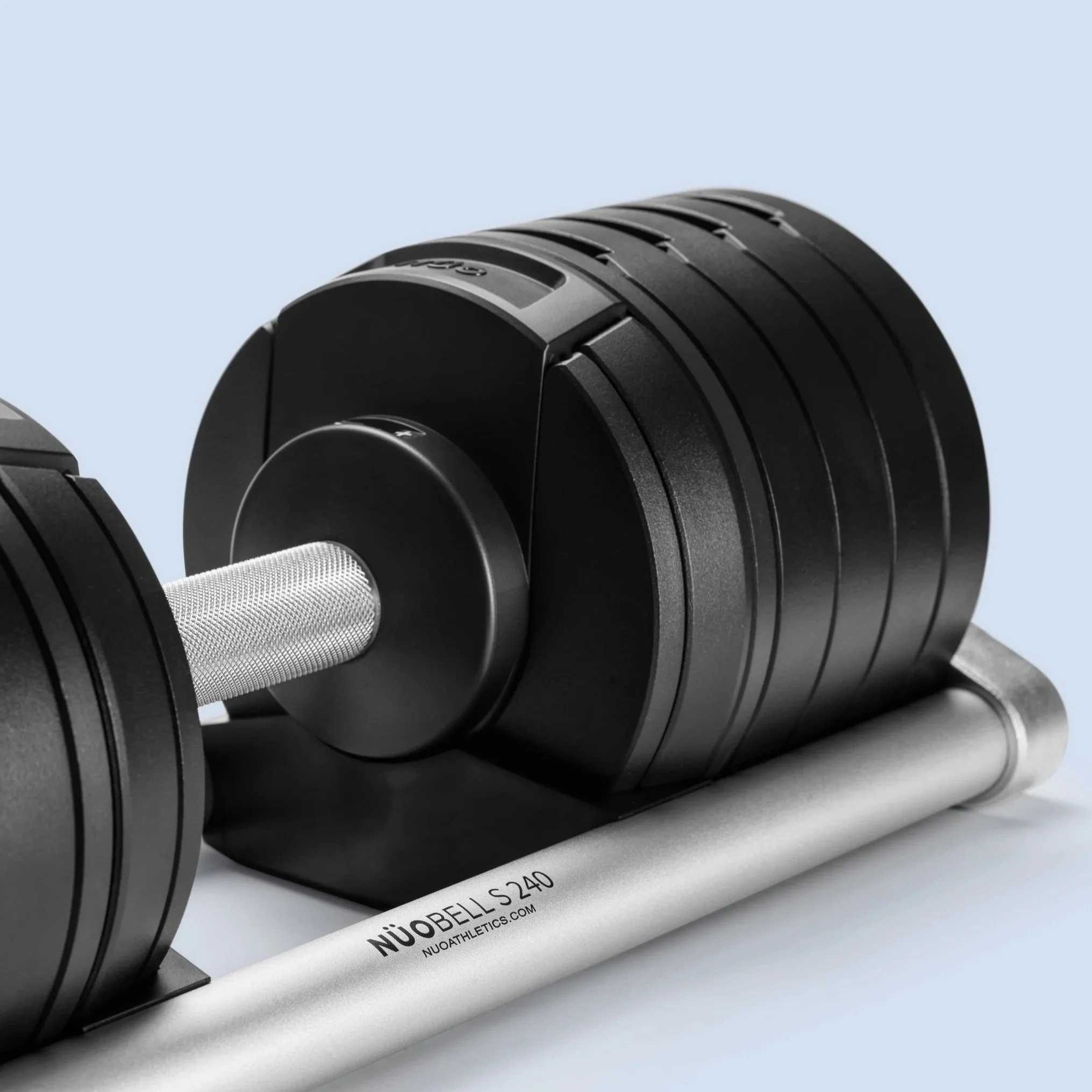 Close-up of a black adjustable dumbbell on a silver weight bar with a light blue background.