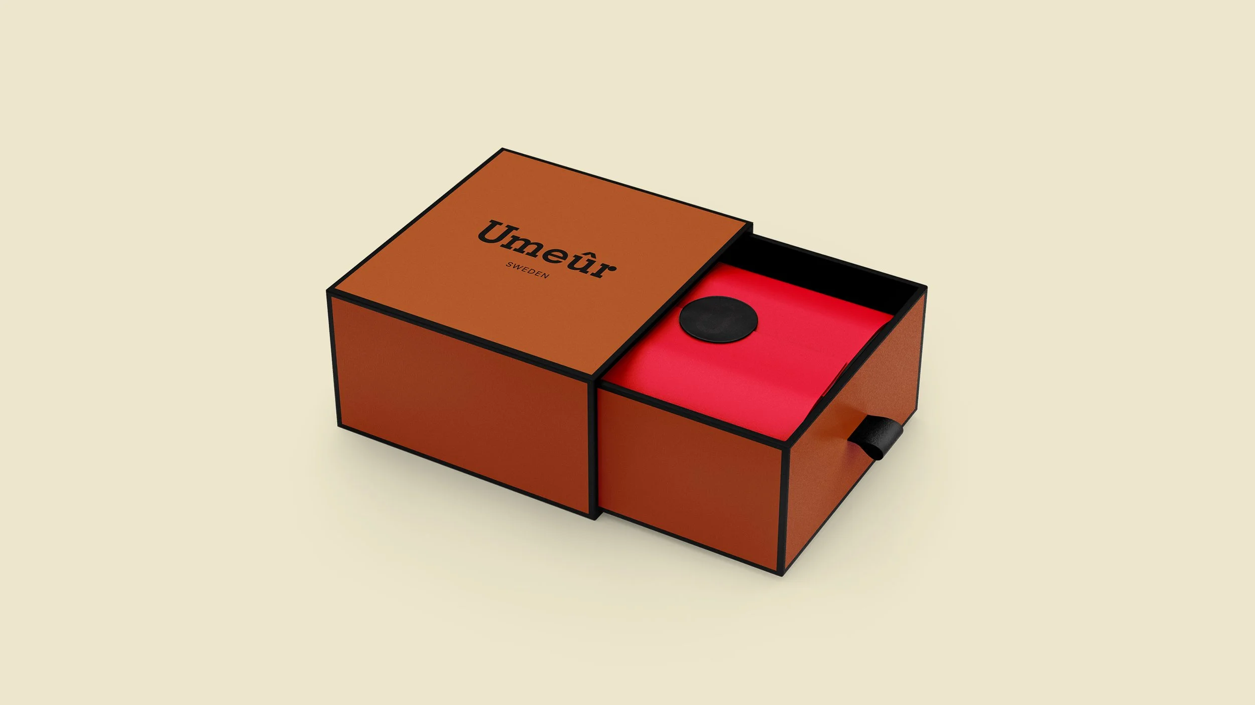 A cardboard box with black outlines labeled 'Umeùr' and 'Sweden,' containing a red object with a black circular detail and a small black tab on the side.
