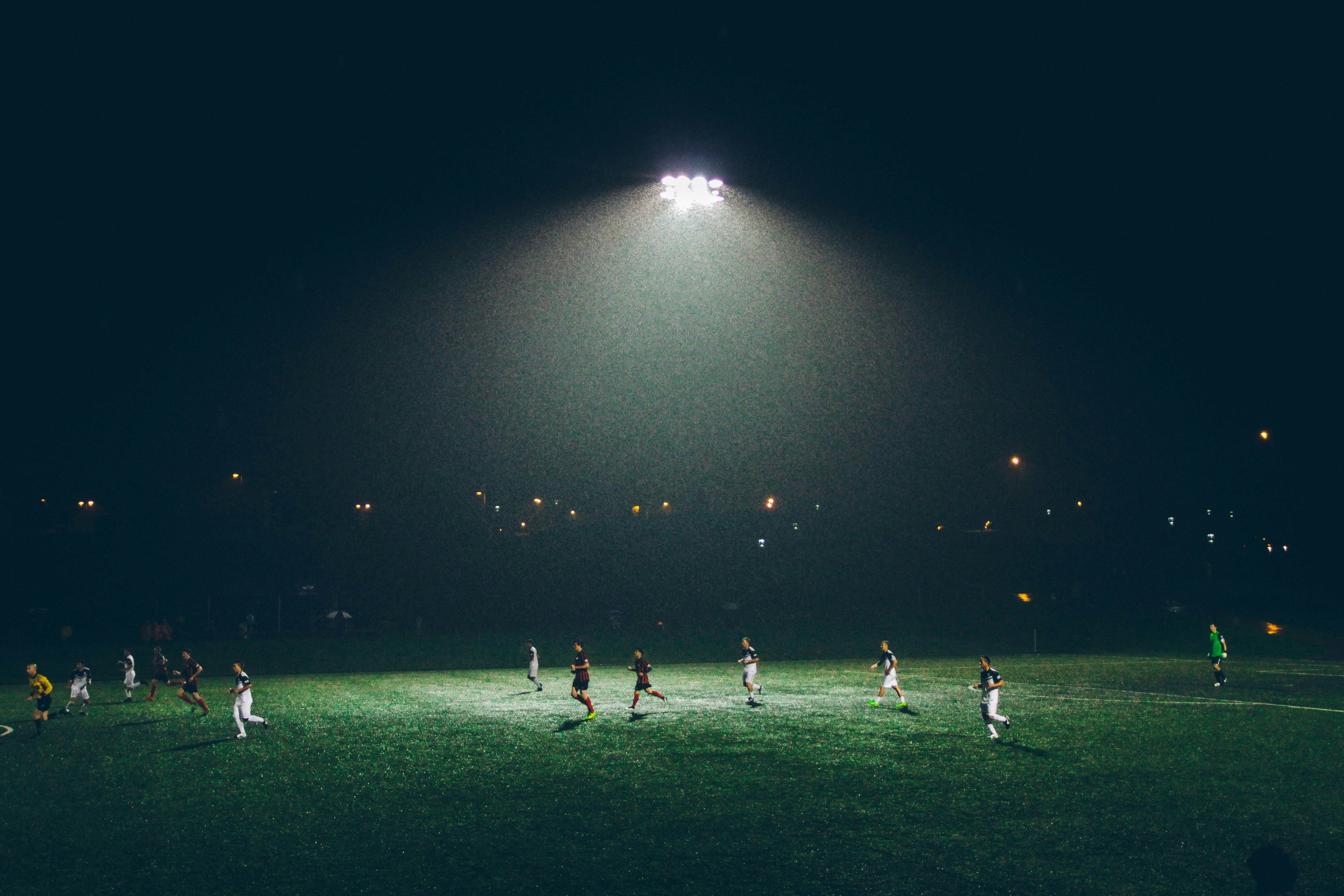 Soccer and football players on a field at night under bright stadium lights.