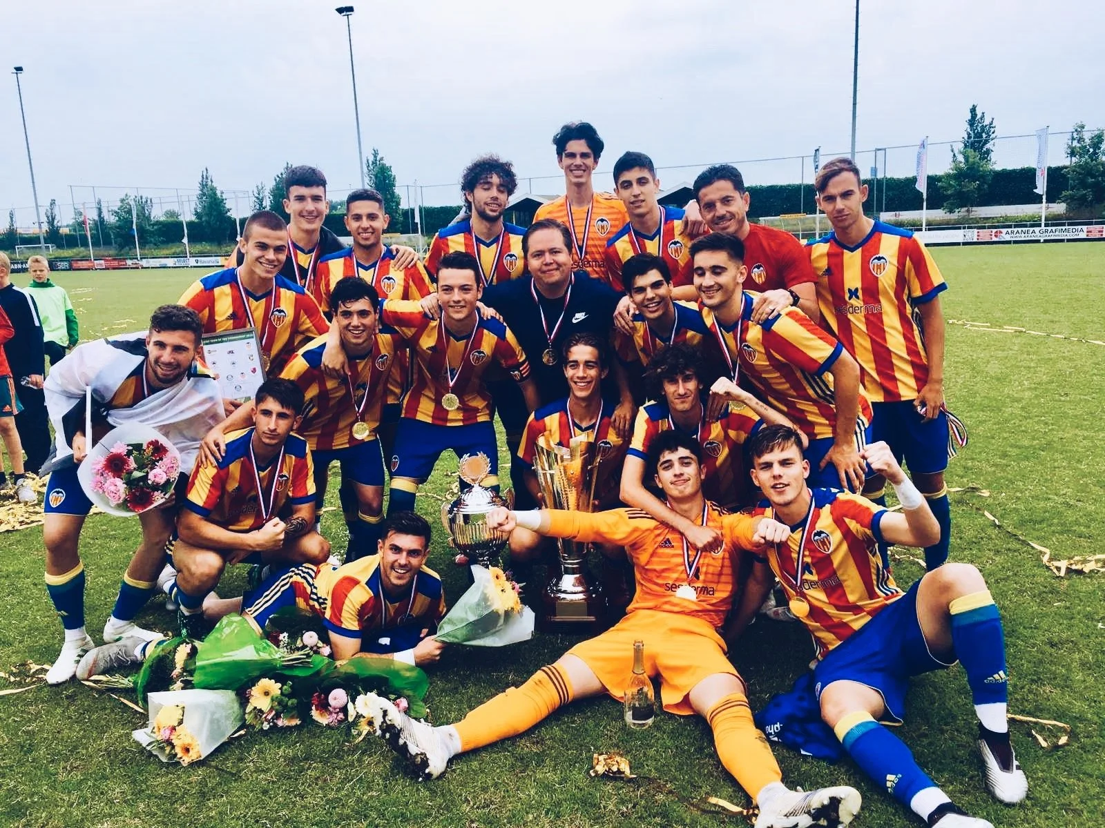 Valencia C.F Football club players in red and yellow striped jerseys celebrating on a soccer field, holding medals, flowers, and trophies. Jaime Gonzalez Albarran, founder of GO-AL in the middle of the team.