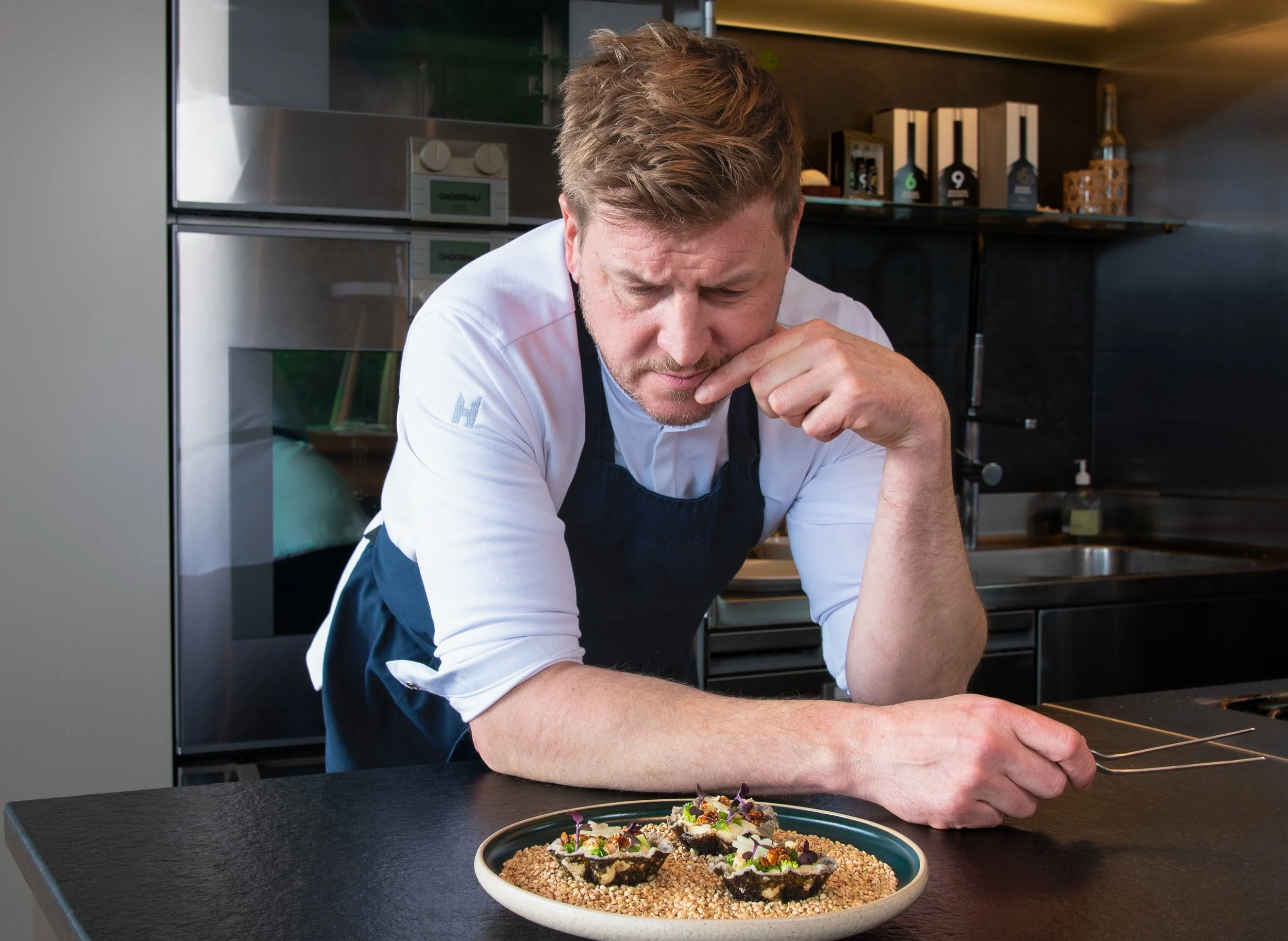 Koch muss ein Gericht auf einem Teller in einer modernen Küche anrichten.