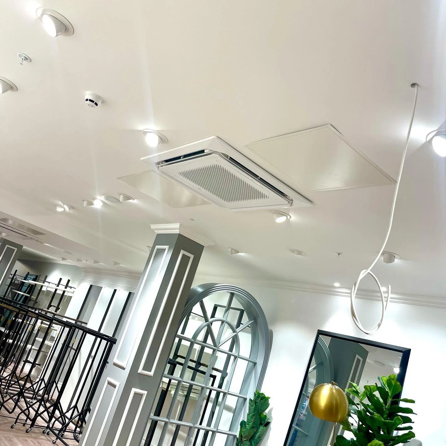 Ceiling with multiple recessed lights, air conditioning vent, and a hanging white wire. Part of an interior room with decorative vertical paneling, plants, and a mirror.