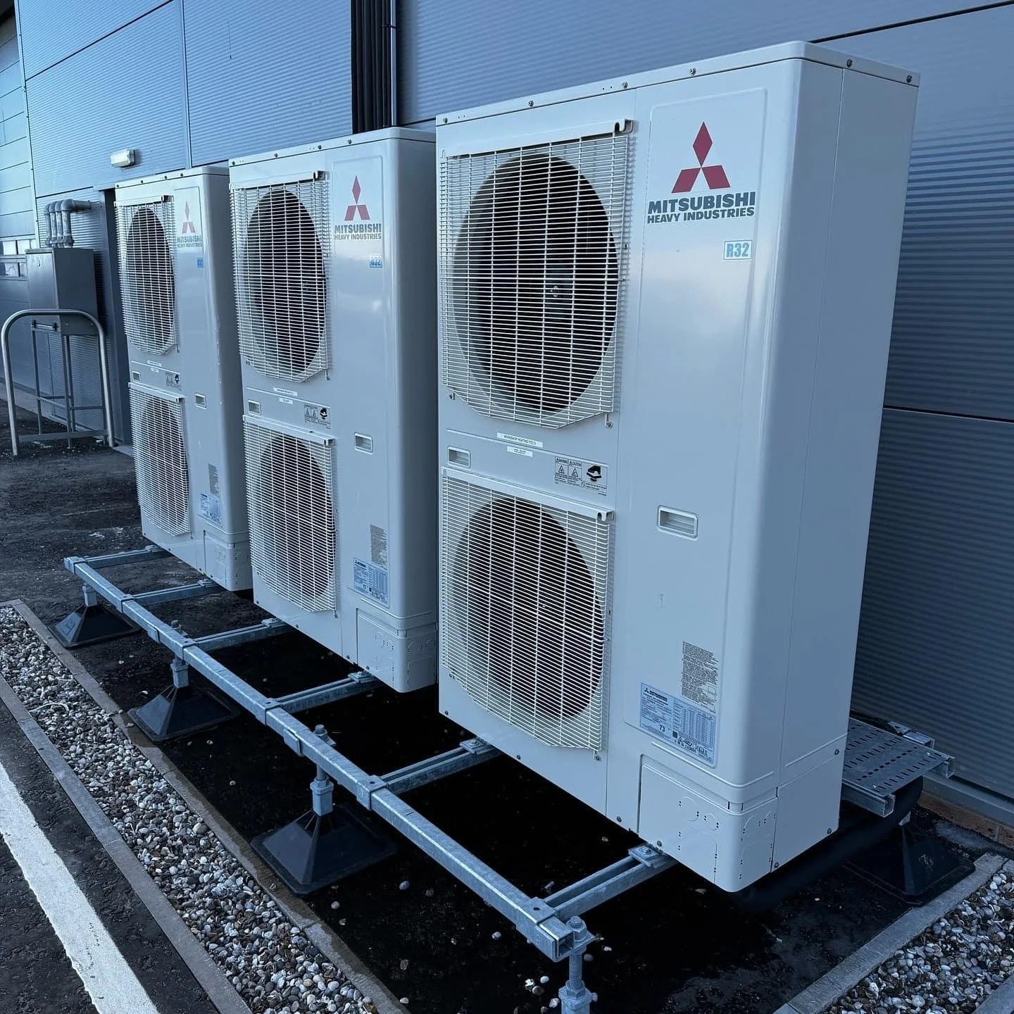 Four Mitsubishi Heavy Industries outdoor air conditioning units installed on a metal stand outside a building.