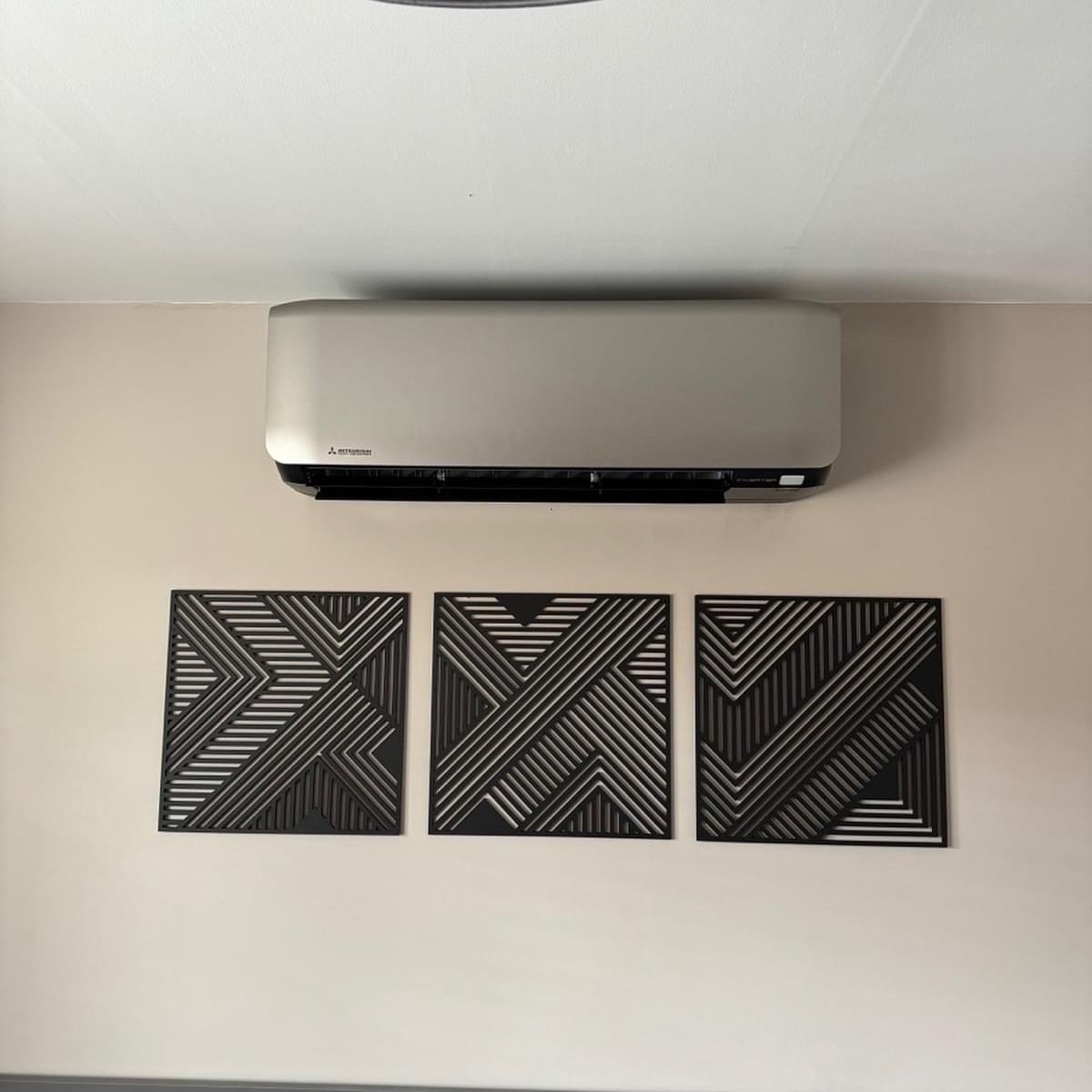 Wall-mounted Mitsubishi air conditioner above three black geometric wall art pieces with striped patterns.