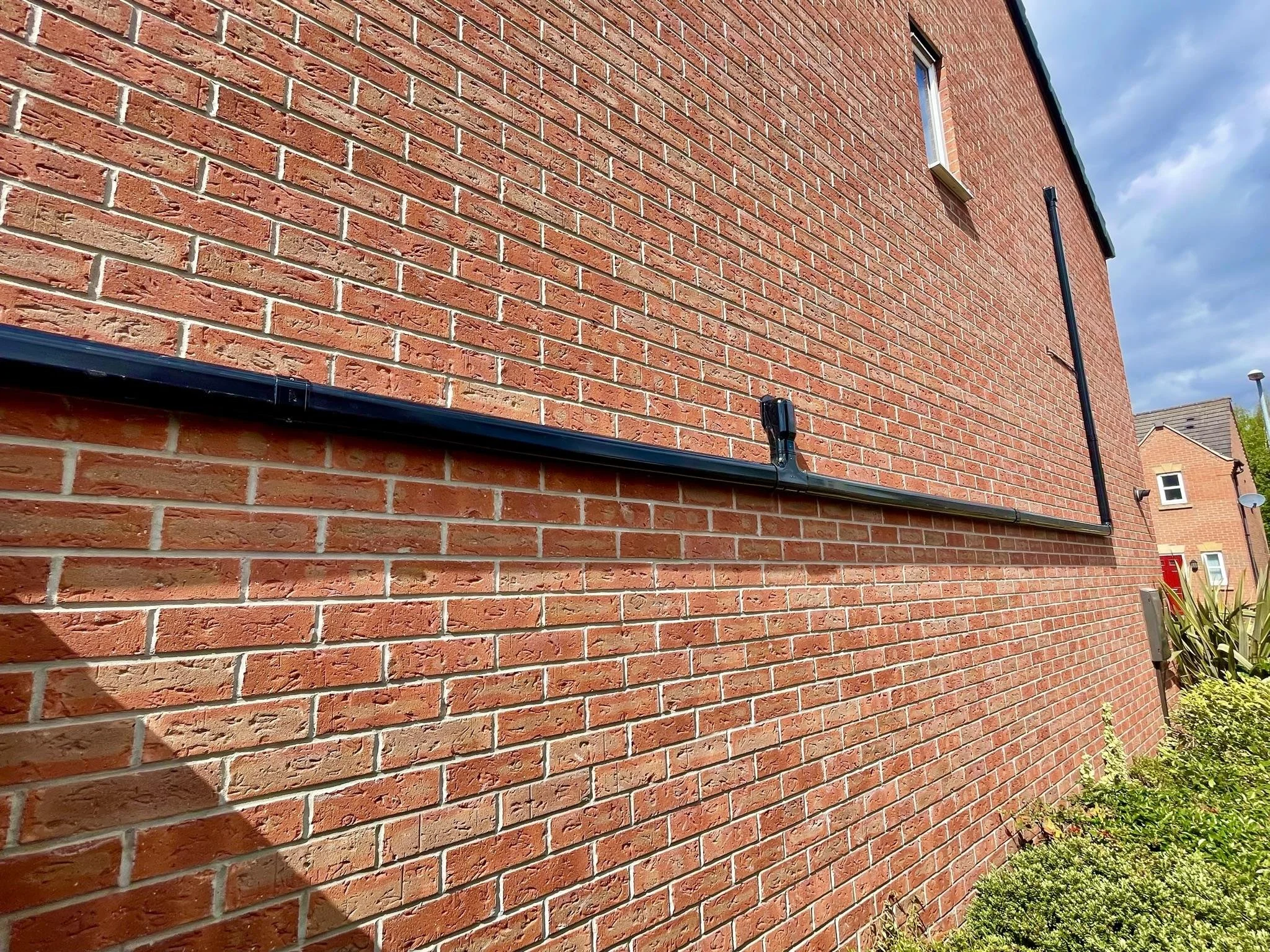 Close-up of a brick house wall with black cable running along it, under a partly cloudy sky.