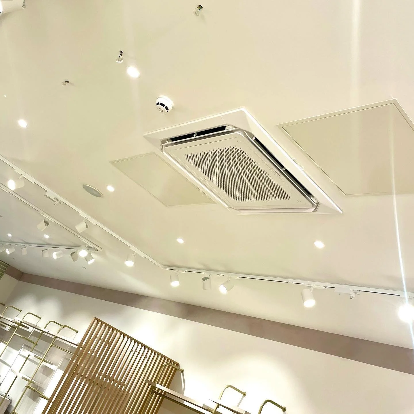 Ceiling with air conditioning unit, fire alarm sensor, and multiple small recessed lights in a modern interior space.