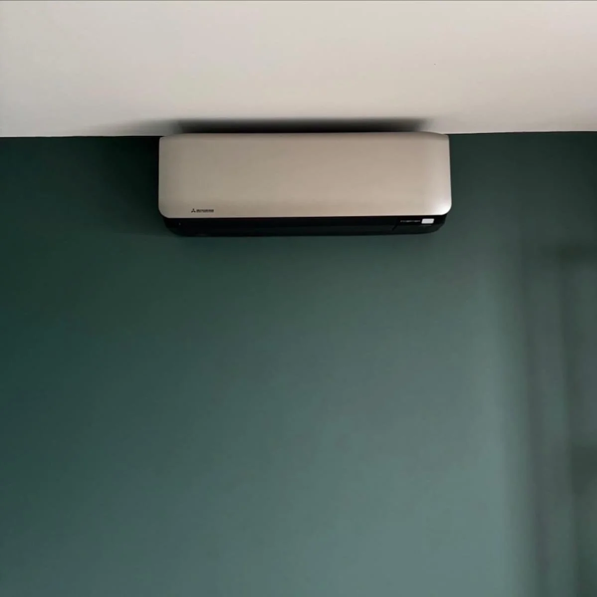 Wall-mounted Mitsubishi air conditioner unit on a green wall.
