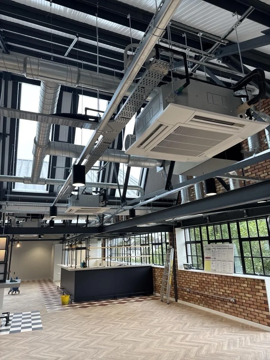 Ceiling with suspended HVAC system and industrial ductwork in a modern open-plan space with large windows and a brick wall.