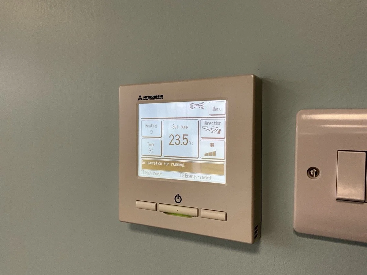 Digital thermostat mounted on a light-colored wall displaying a temperature setting of 23.5 degrees Celsius.