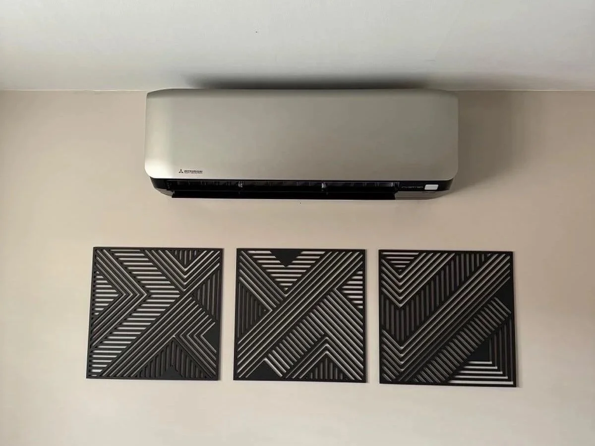 A wall-mounted Mitsubishi air conditioning unit above three black decorative wall panels with geometric patterns.