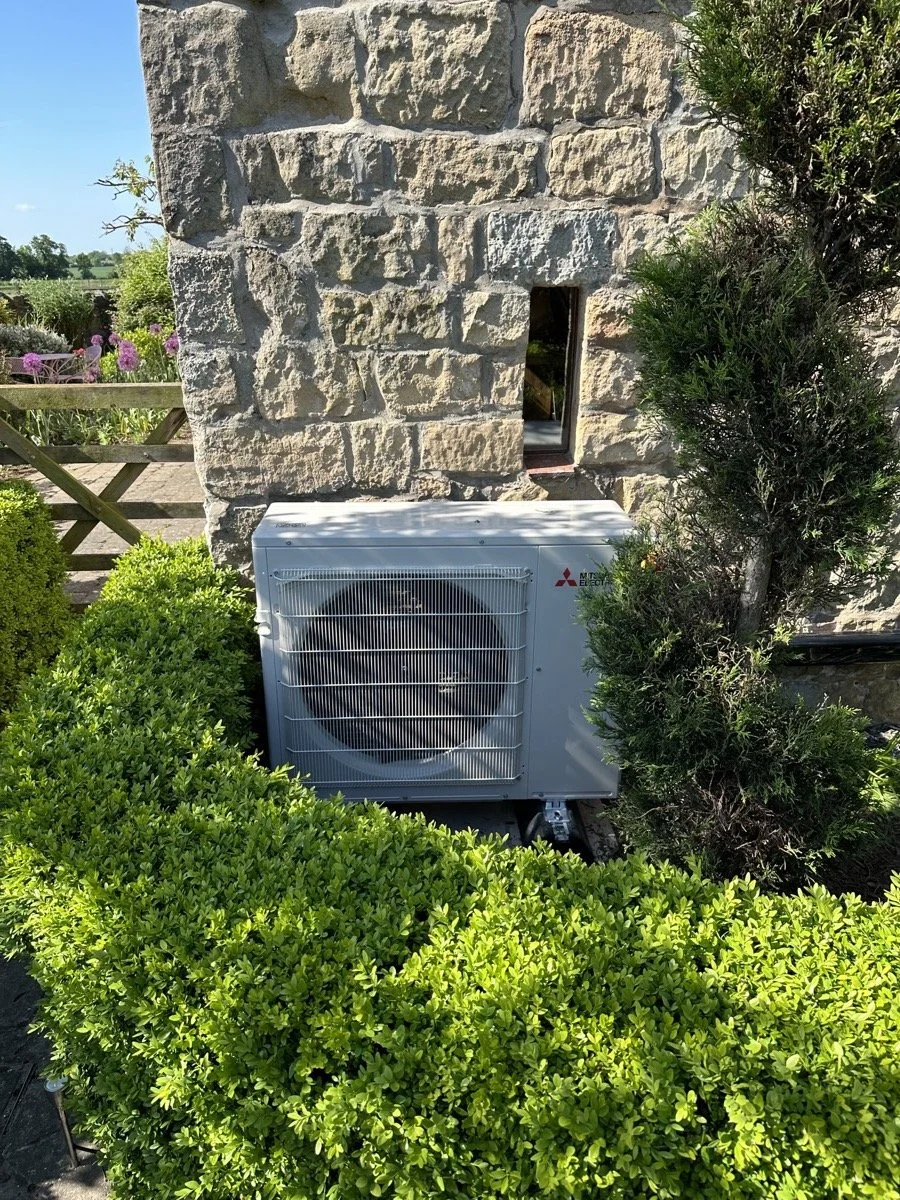 Outdoor scene with a stone wall, bushes, and a Mitsubishi air conditioning unit.