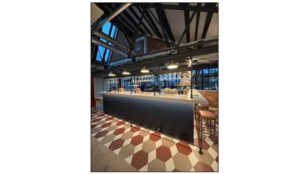 Modern restaurant interior with a black counter, industrial lighting, large windows, and patterned tile floor.