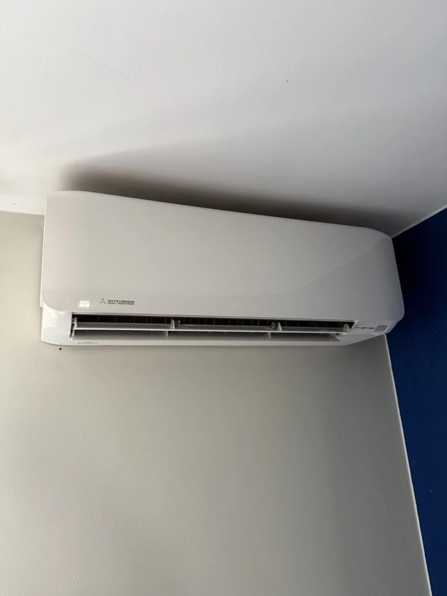 Wall-mounted Mitsubishi air conditioner unit in a room with cream-colored and blue walls.