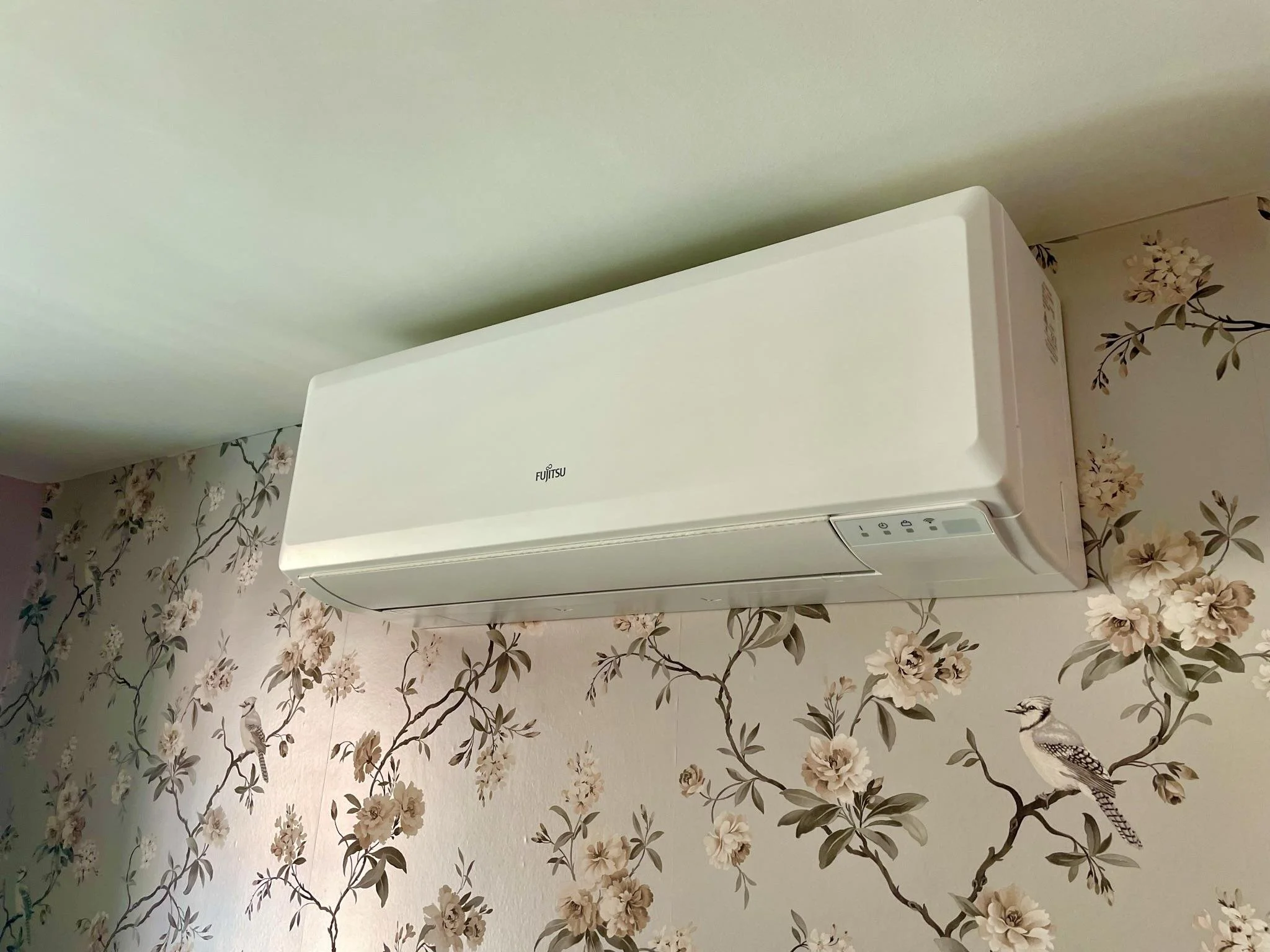 White Fujitsu wall-mounted air conditioner unit installed on a floral patterned wall with bird and flower artwork.