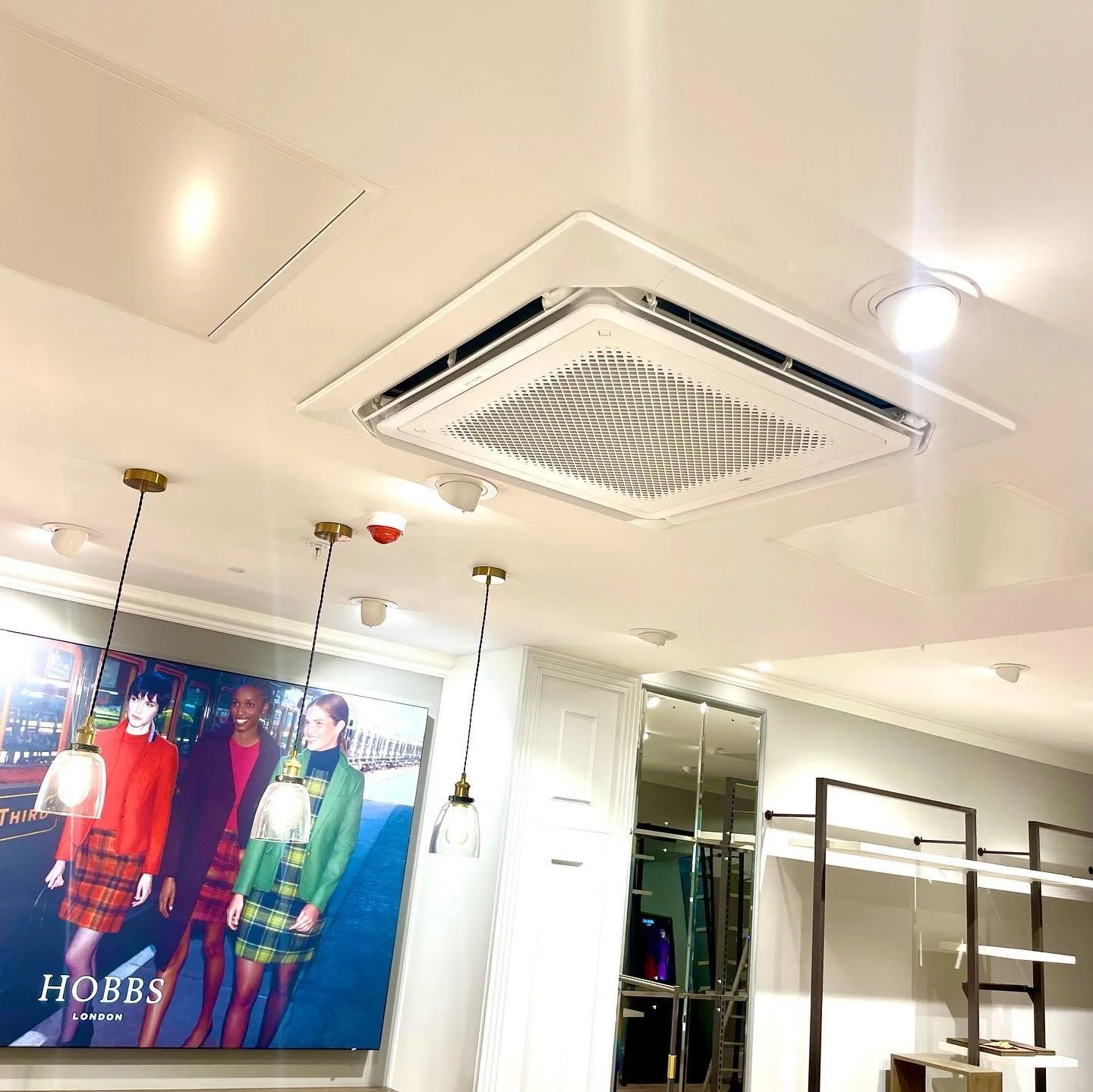 Ceiling with built-in air conditioning vent, two ceiling lights, and hanging pendant light, with clothing store displays and mannequins in the background.