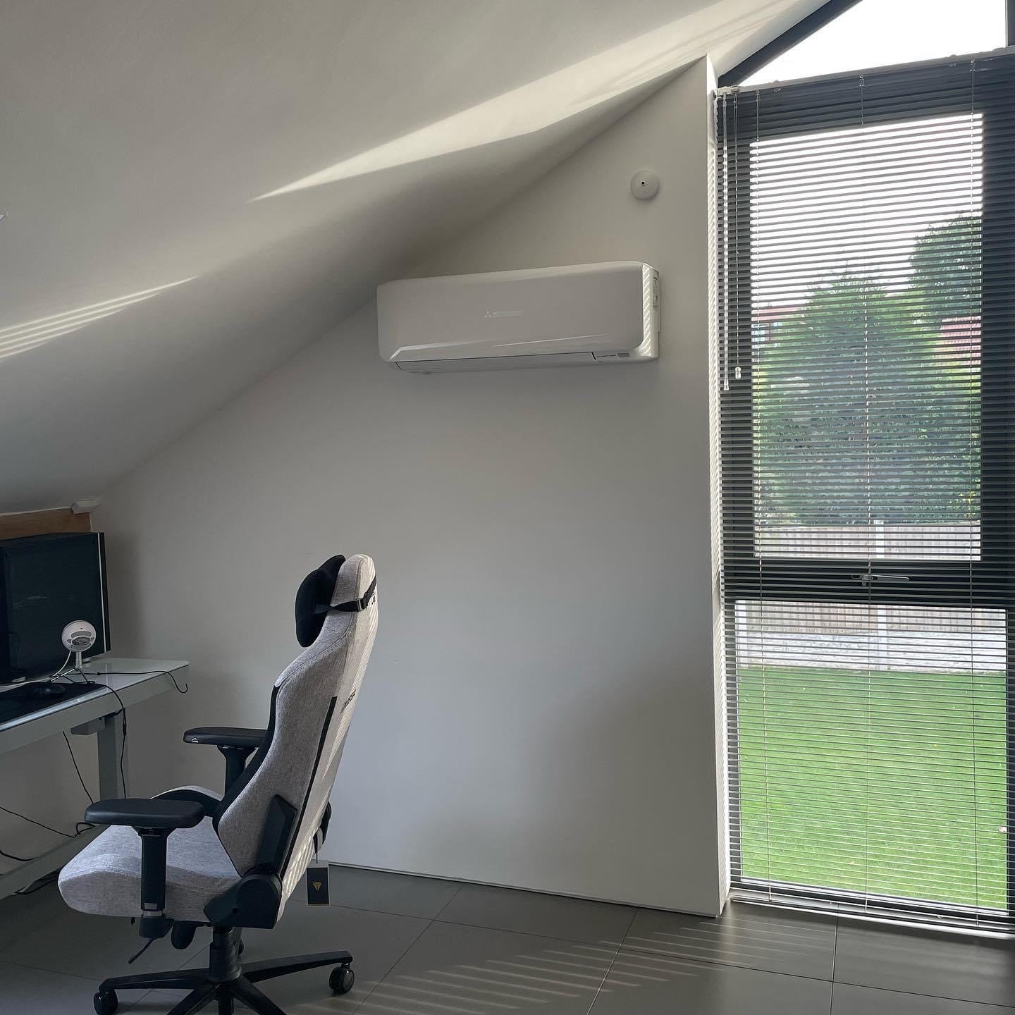 Home office with a gray office chair, a desk, computer monitor, and a window with blinds, and a wall-mounted air conditioner.