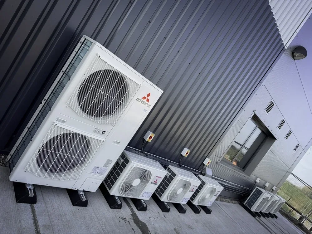 Multiple Mitsubishi HVAC units installed outside a building on a concrete surface, with electrical connections and vents visible.