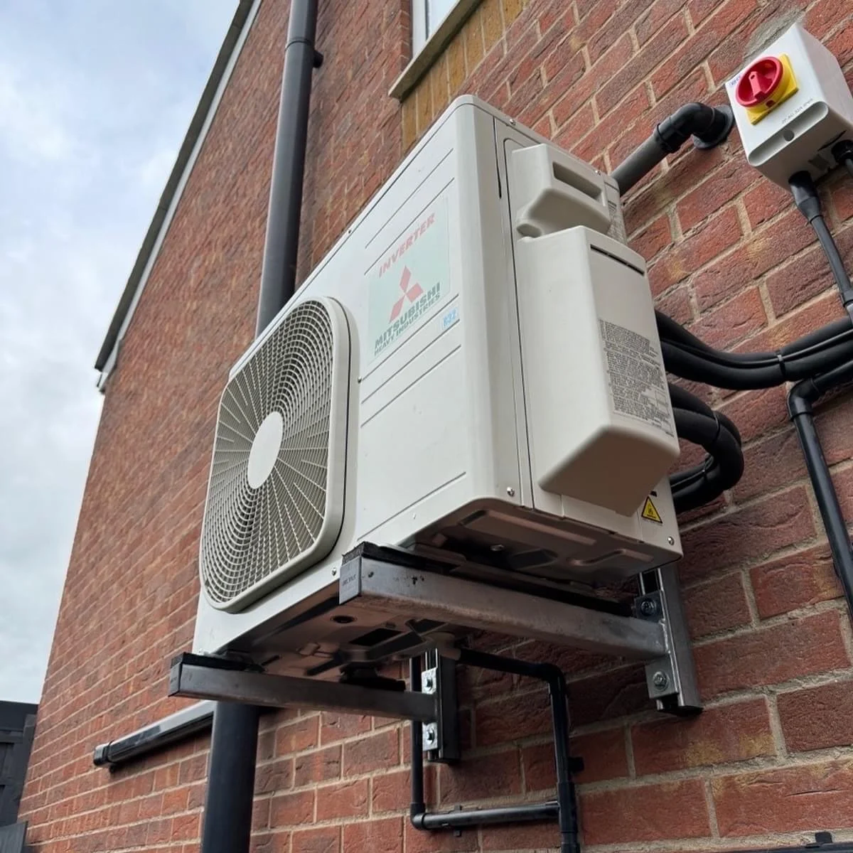 Outdoor Mitsubishi air conditioning unit mounted on a metal bracket on a brick wall.