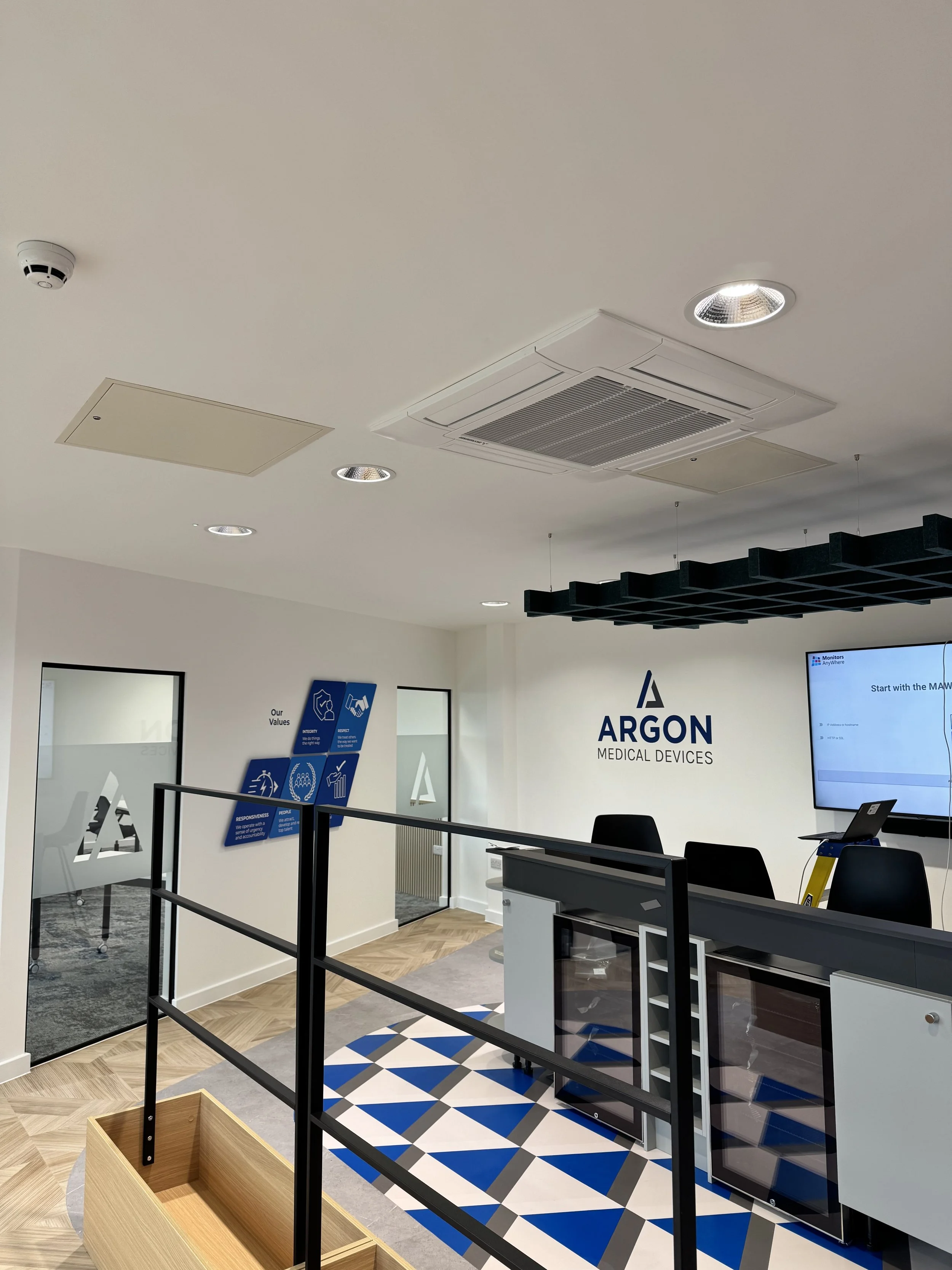 Reception area of Argon Medical Devices office with a large wall mounted screen, a reception desk, chairs, and signage on the wall.