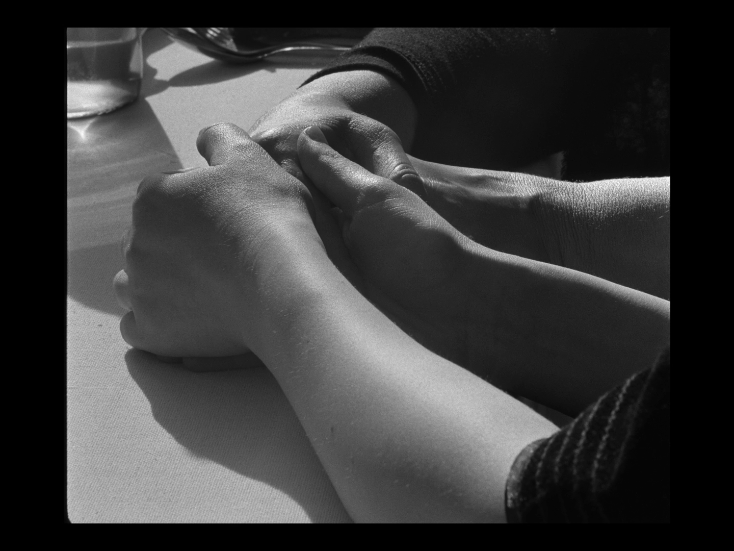 Close-up black and white photo of two pairs of hands holding each other on a table.