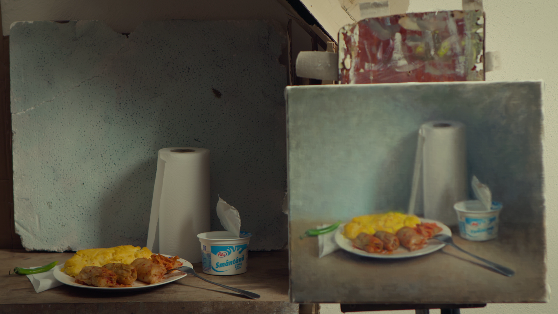 A tabletop scene with a plate of scrambled eggs, sausages, a fork, a green chili, a container of yogurt, a paper towel roll, and a torn wall with a mirror reflecting the scene.