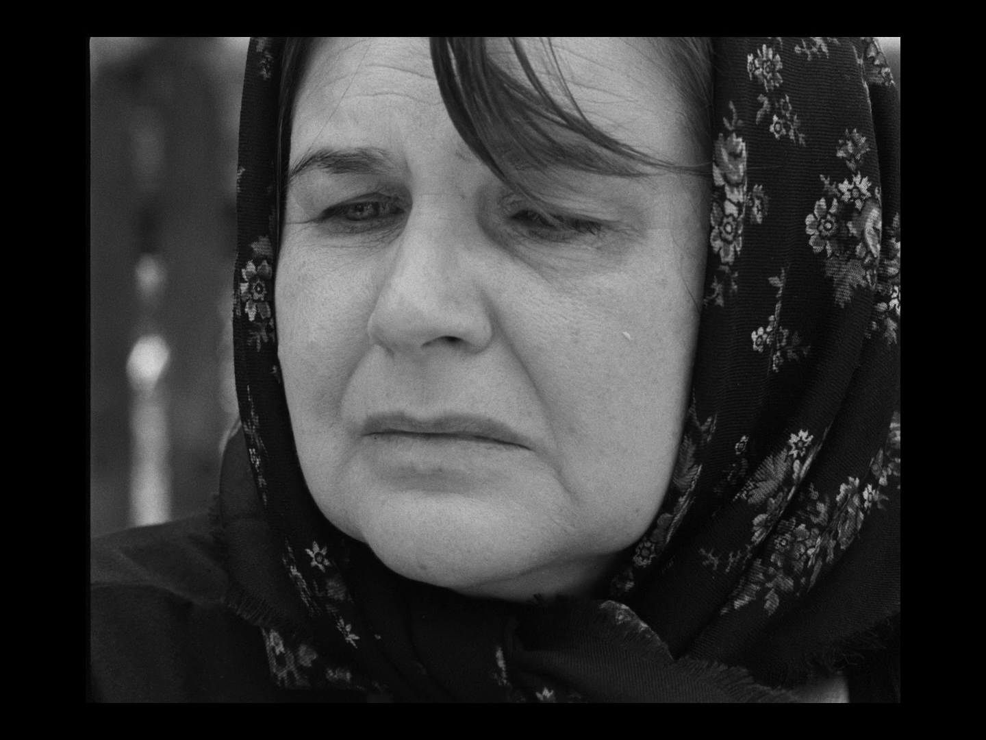A woman with a scarf around her head, looking slightly to the side with a serious expression.