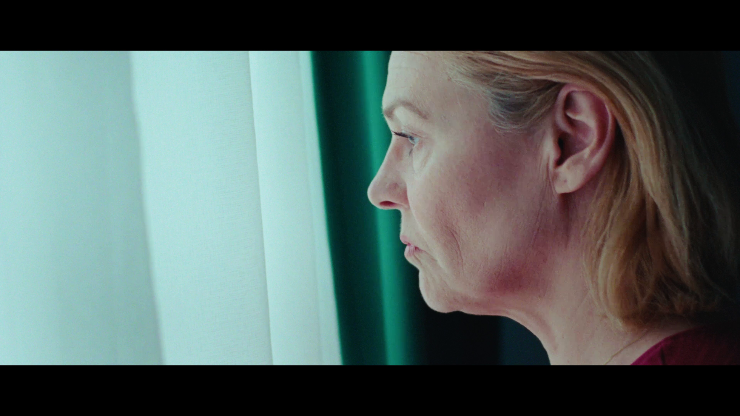 Close-up of a woman with blonde hair looking out a window in profile view.