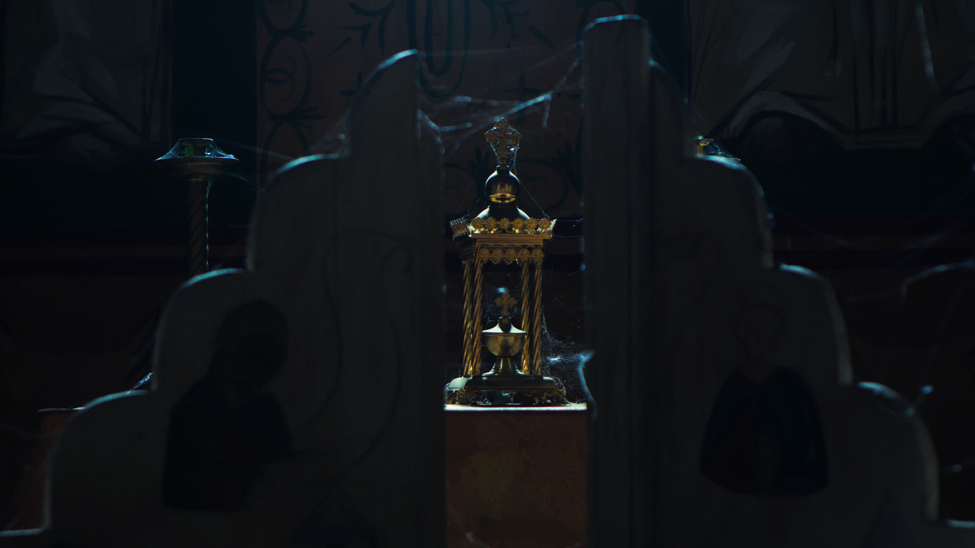 Dimly lit room with a central ornate religious or ceremonial object, surrounded by cutouts of human figures on chairs, with cobwebs indicating abandonment.