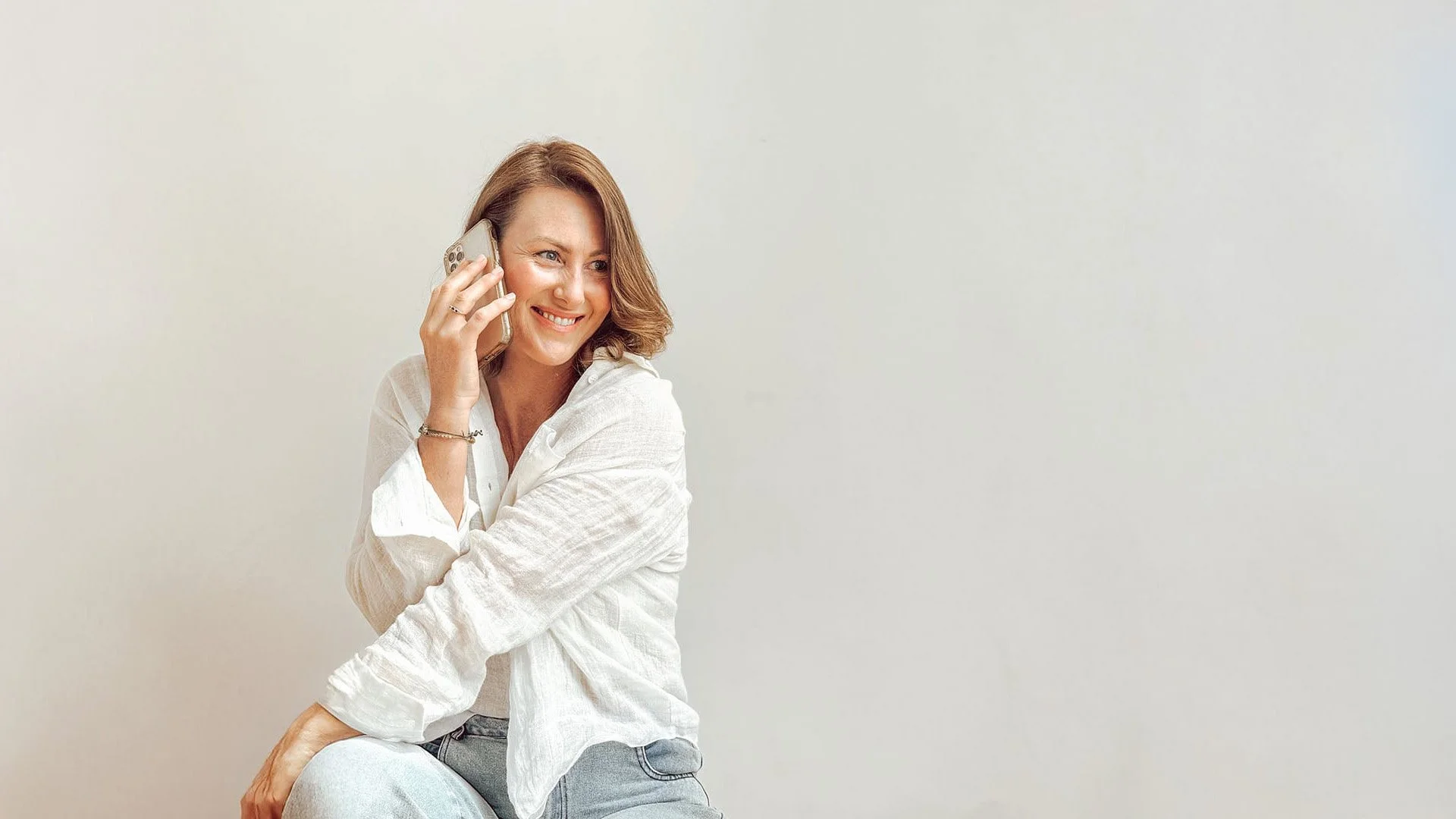 Portrait of Lauren Rosser, Meta Ads Strategist talking on a mobile phone, wearing a white linen shirt and smiling.