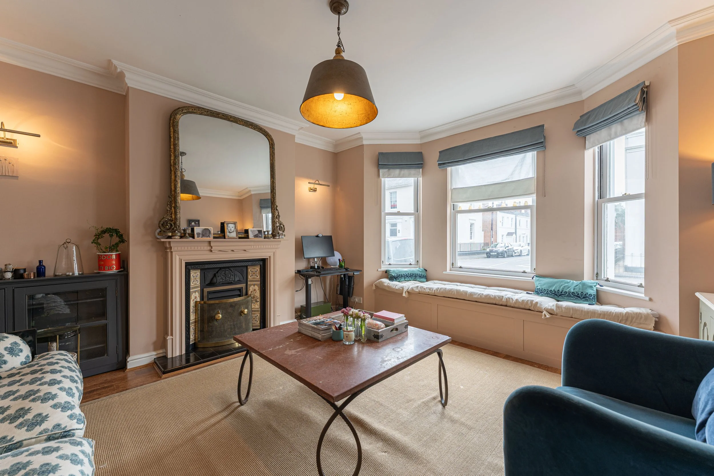 Living room with a beige wall, windows with blue shades, a fireplace with a large mirror above, a beige sofa, a dark armchair, a mid-sized coffee table, and a beige carpet.