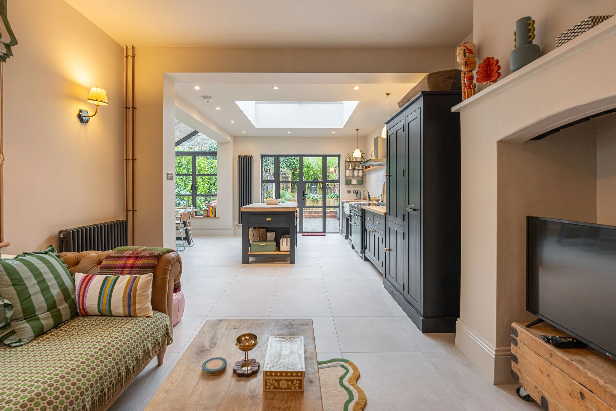 Open-concept living room and kitchen with black cabinetry, a skylight, large windows, and a sliding glass door leading outside.
