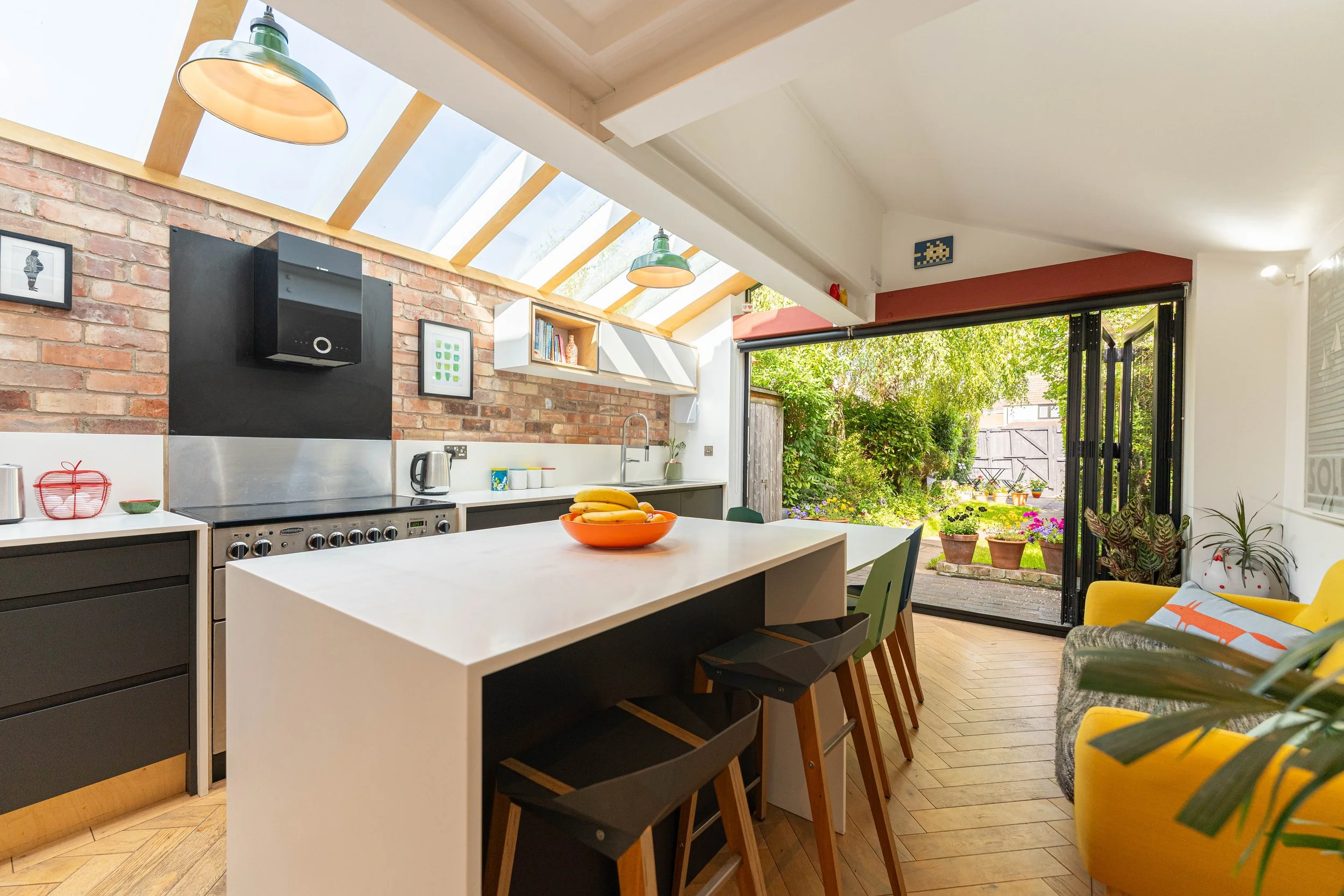 Bright modern kitchen with a white island, black cabinetry, a brick accent wall, and large glass doors leading to a lush garden.