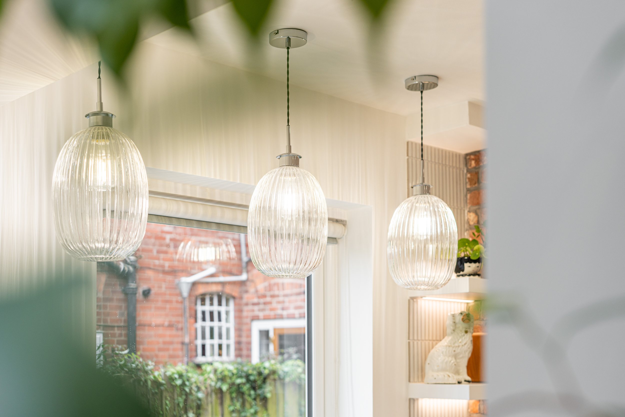 Three hanging glass pendant lights inside a room with a window showing a brick building outside.