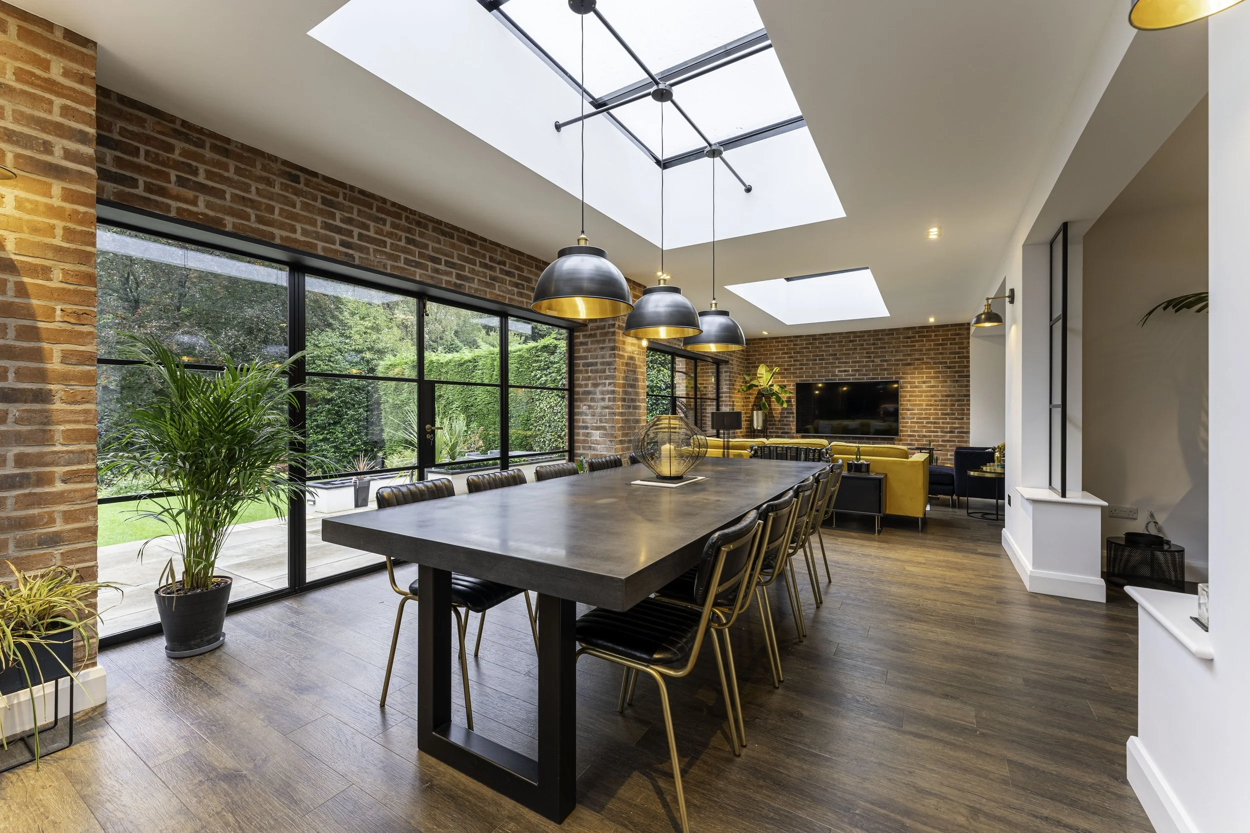 Modern dining and living area with brick walls, large windows, wood flooring, and black and yellow furniture.