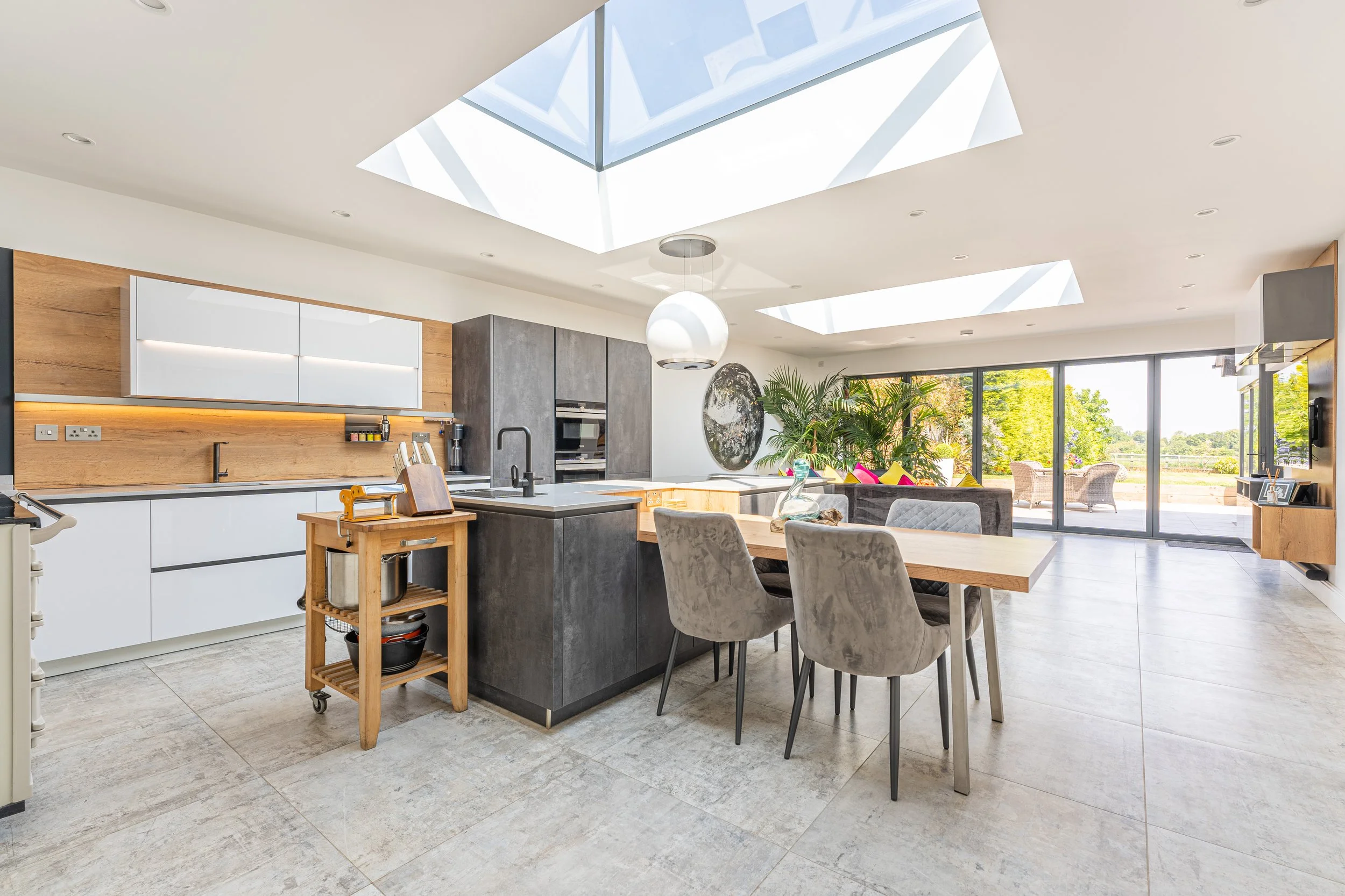 Modern open-concept kitchen and dining area with large skylights, sliding glass doors, and a view of outdoor patio with seating.
