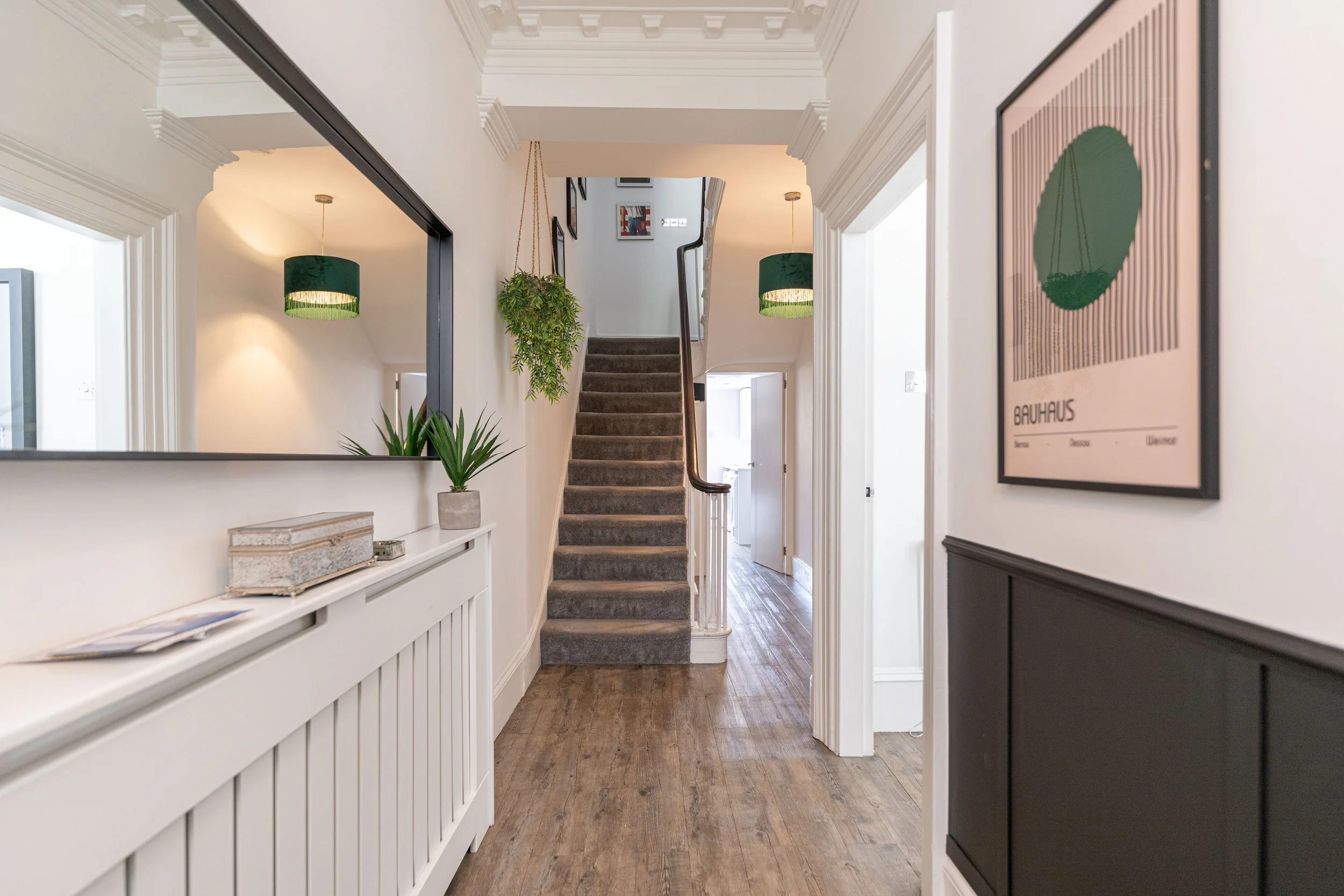 Entryway with stairs, hardwood flooring, plants, mirror, hanging lights, and framed artwork.