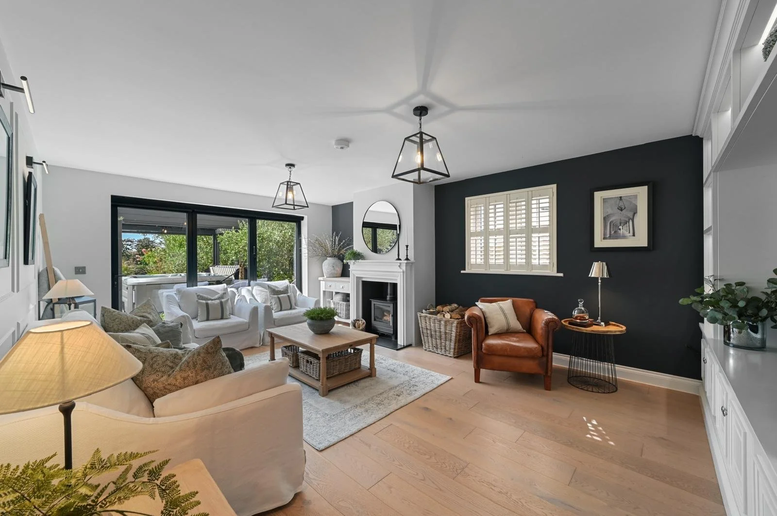 Living room with a black accent wall, white sofas, a brown leather armchair, a fireplace, large sliding glass doors, and wooden flooring.