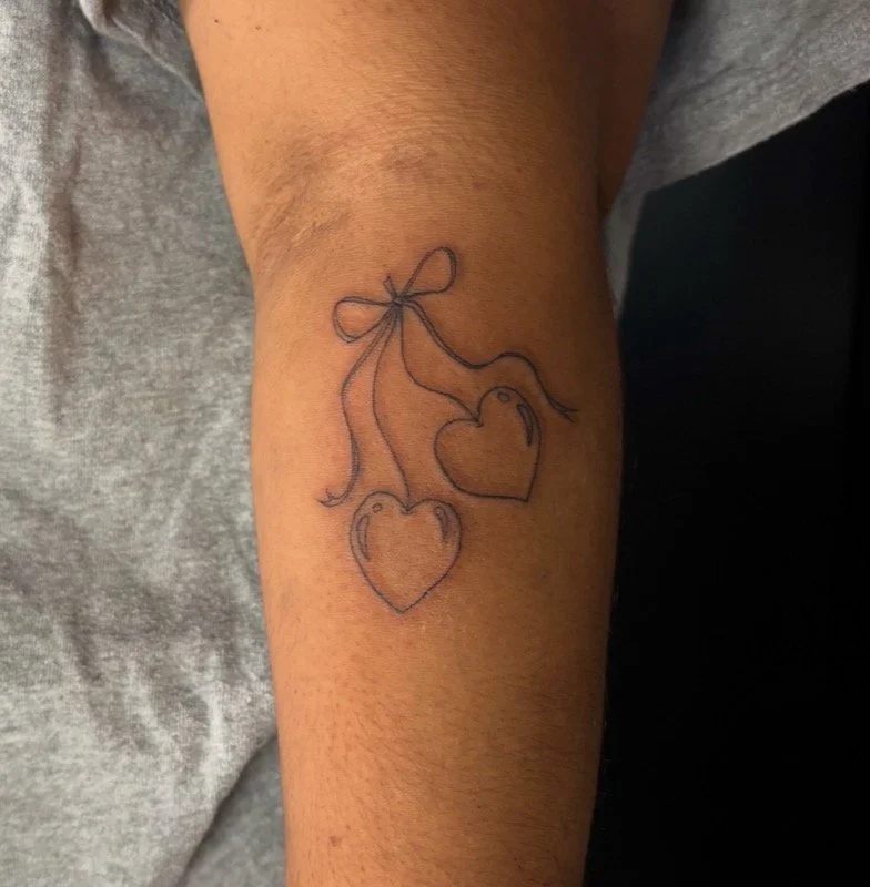 Fine line tattoo of two hearts portrayed as cherries.