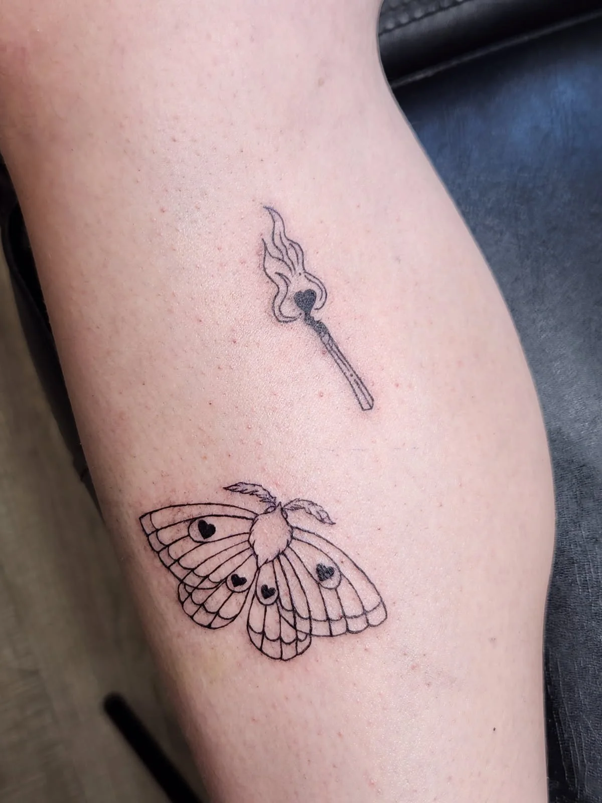 Two fine line tattoos. One of a moth with hearts in its patten, the other of a burning match with a heart as the head.