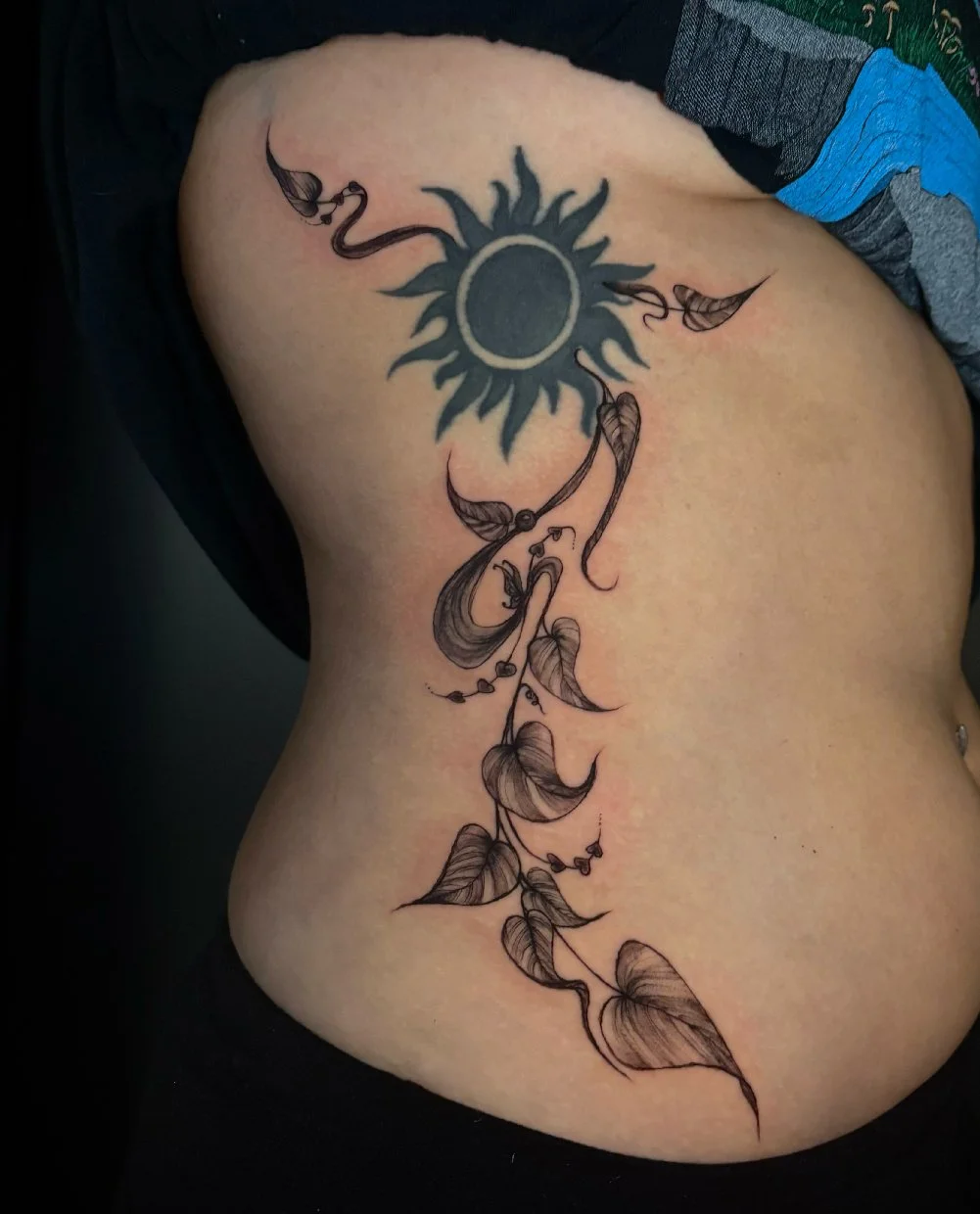 Big tattoo of ivy leaves stemming from an older tattoo of the sun.