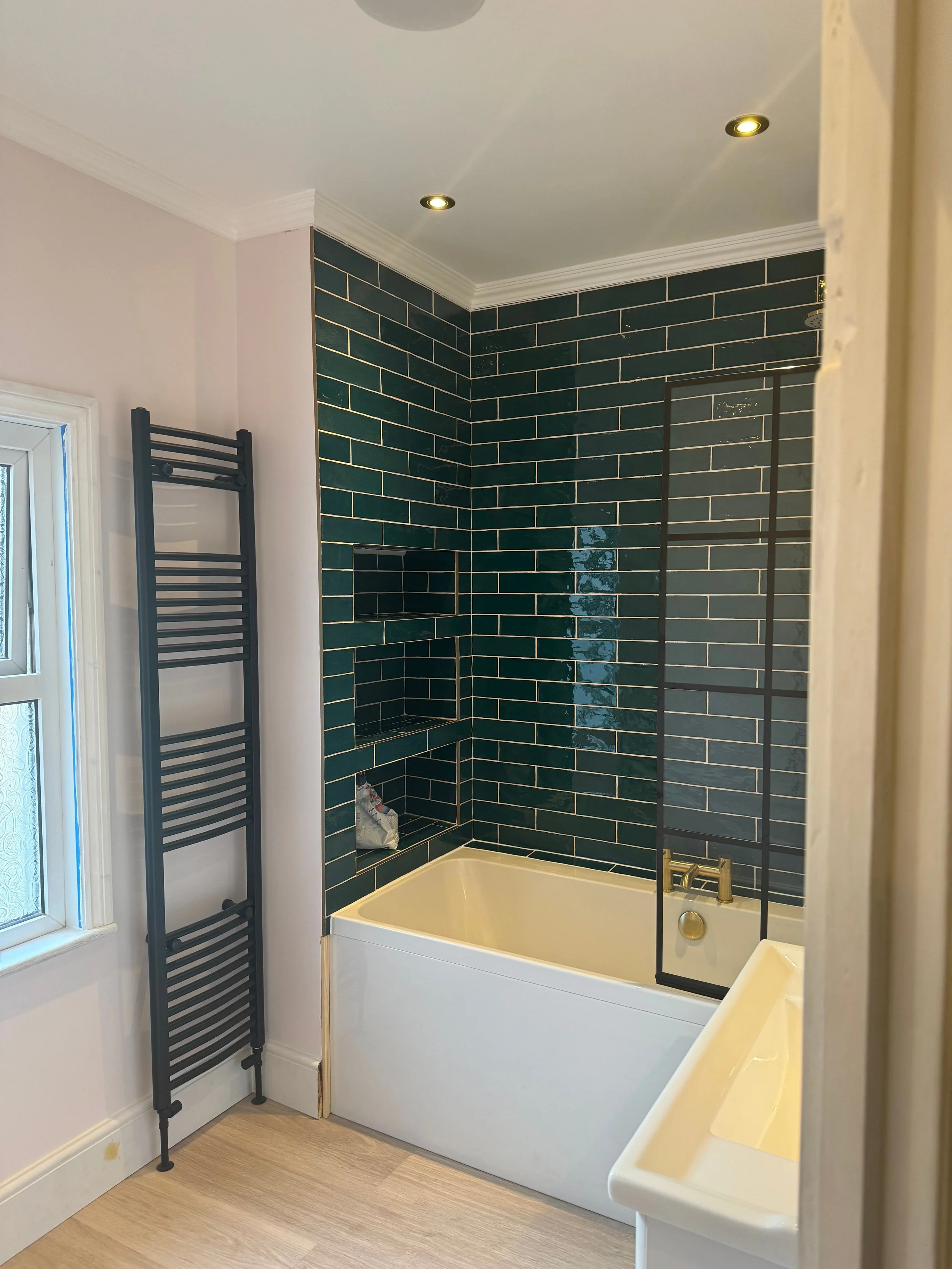 Bathroom with a bathtub, dark green tiled wall, and a black shower screen.
