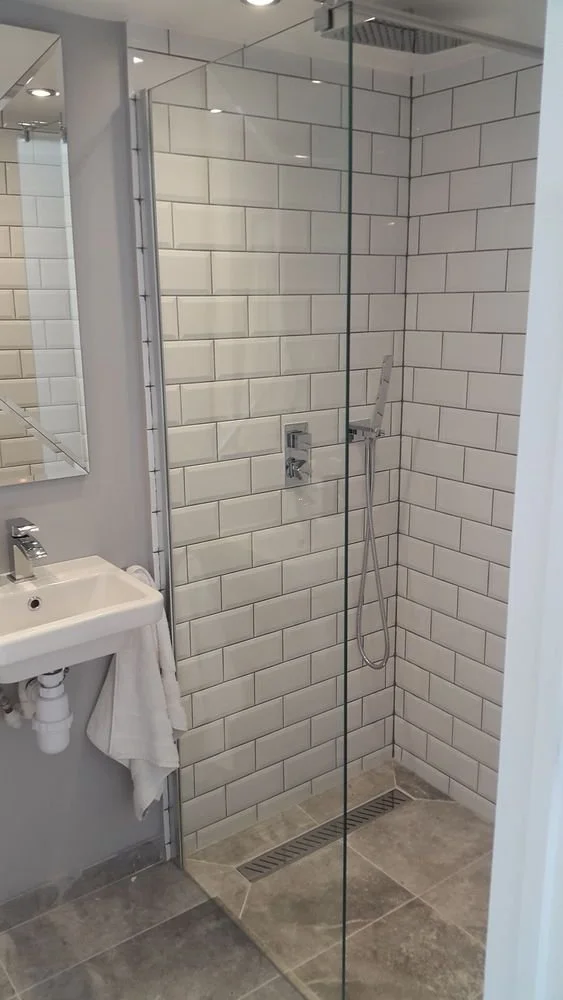 A modern bathroom shower with glass enclosure, white subway tiles, and a handheld showerhead.