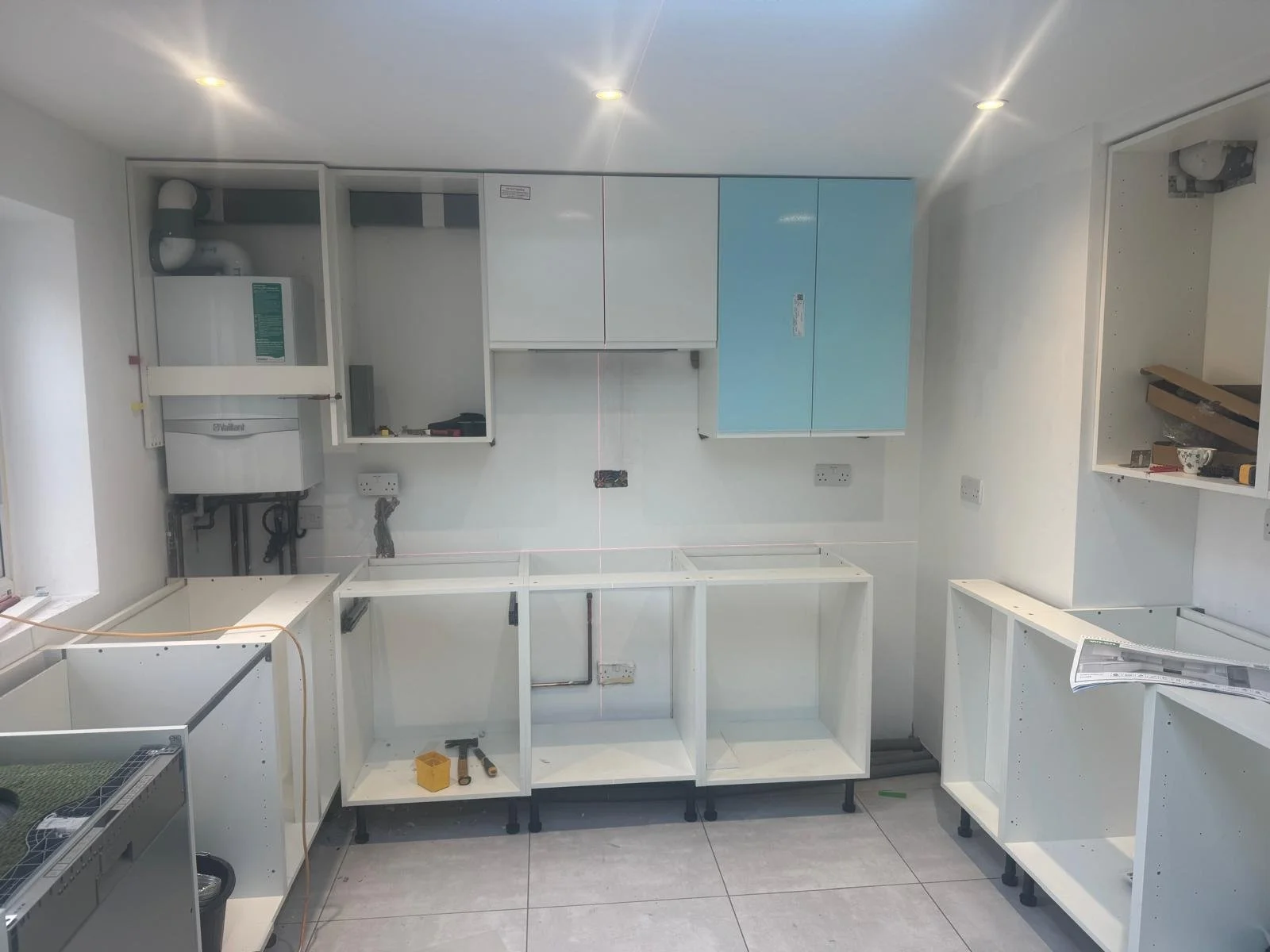 Room under renovation with white cabinets and drawers, some installed and others still being assembled, with tools and construction materials visible.