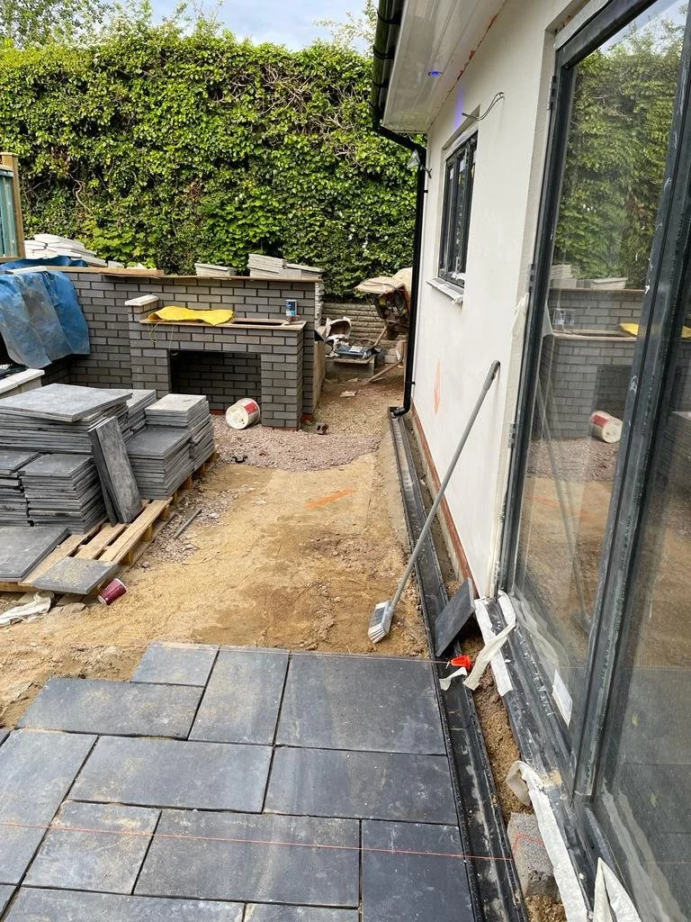 Undergoing outdoor construction, partially installed sliding glass door and newly laid gray paving stones, with construction tools and materials scattered around.