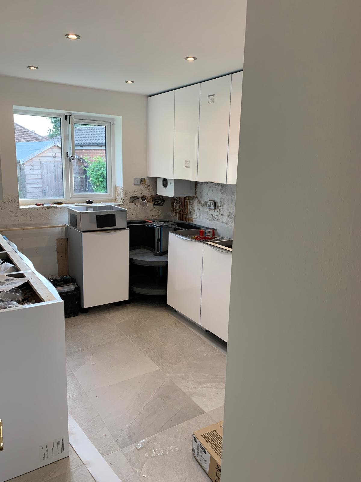 Kitchen under construction with white cabinets, a window, and partially installed appliances and fixtures.