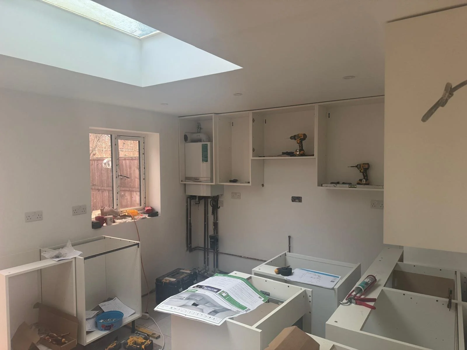 Kitchen under renovation with white cabinets, tools, and construction materials scattered around.