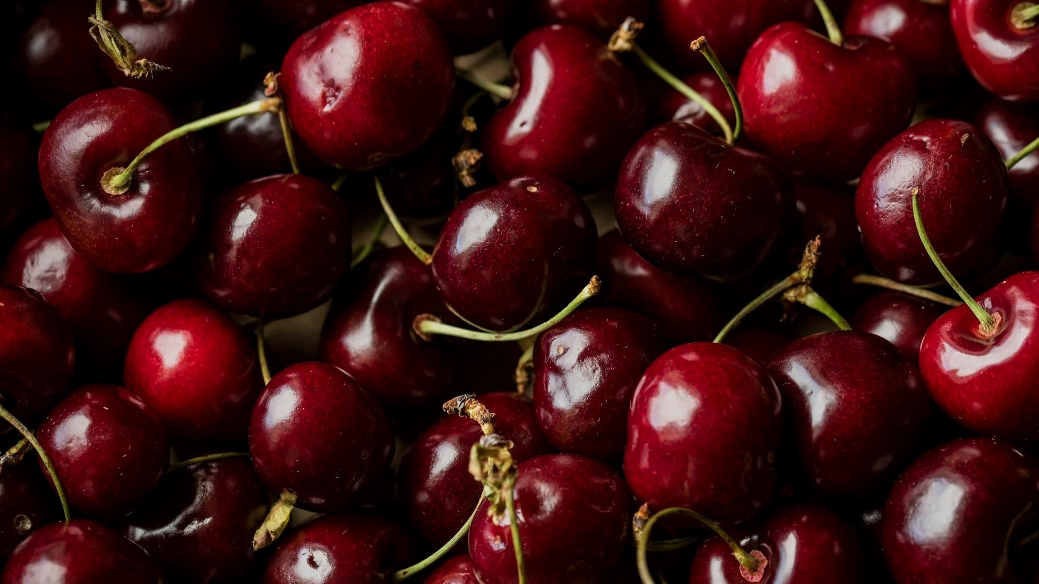 Close-up of a pile of fresh red cherries with green stems.