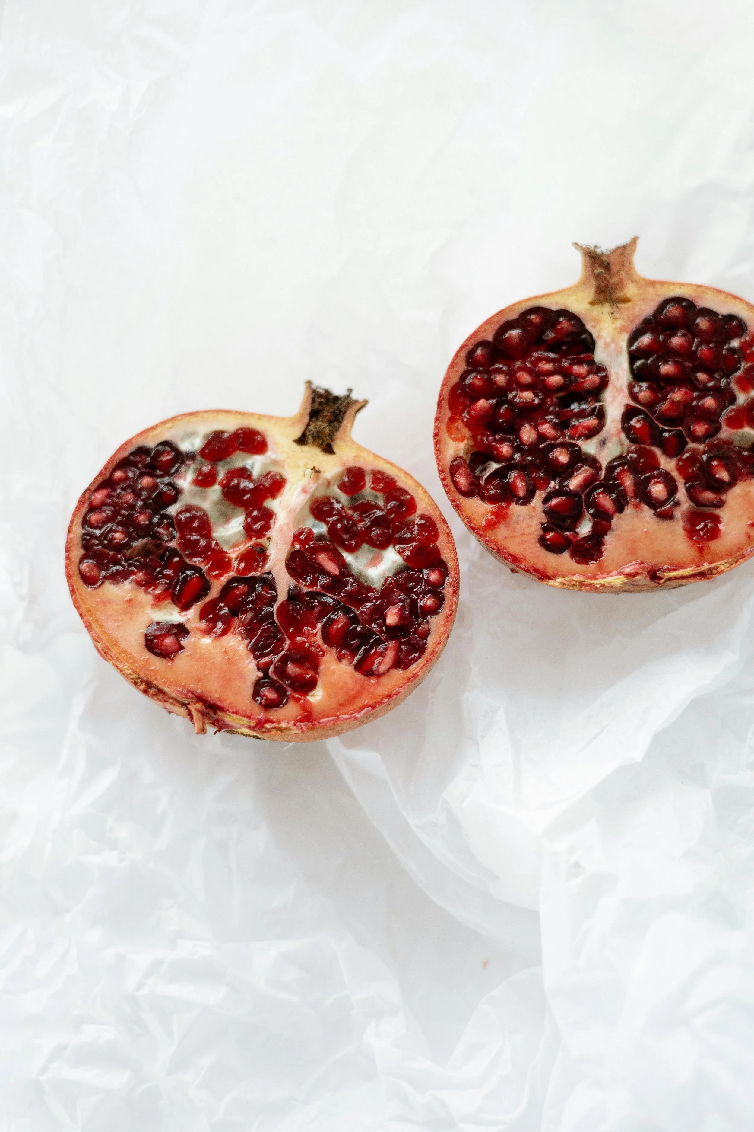 A halved pomegranate with red seeds on white tissue paper.