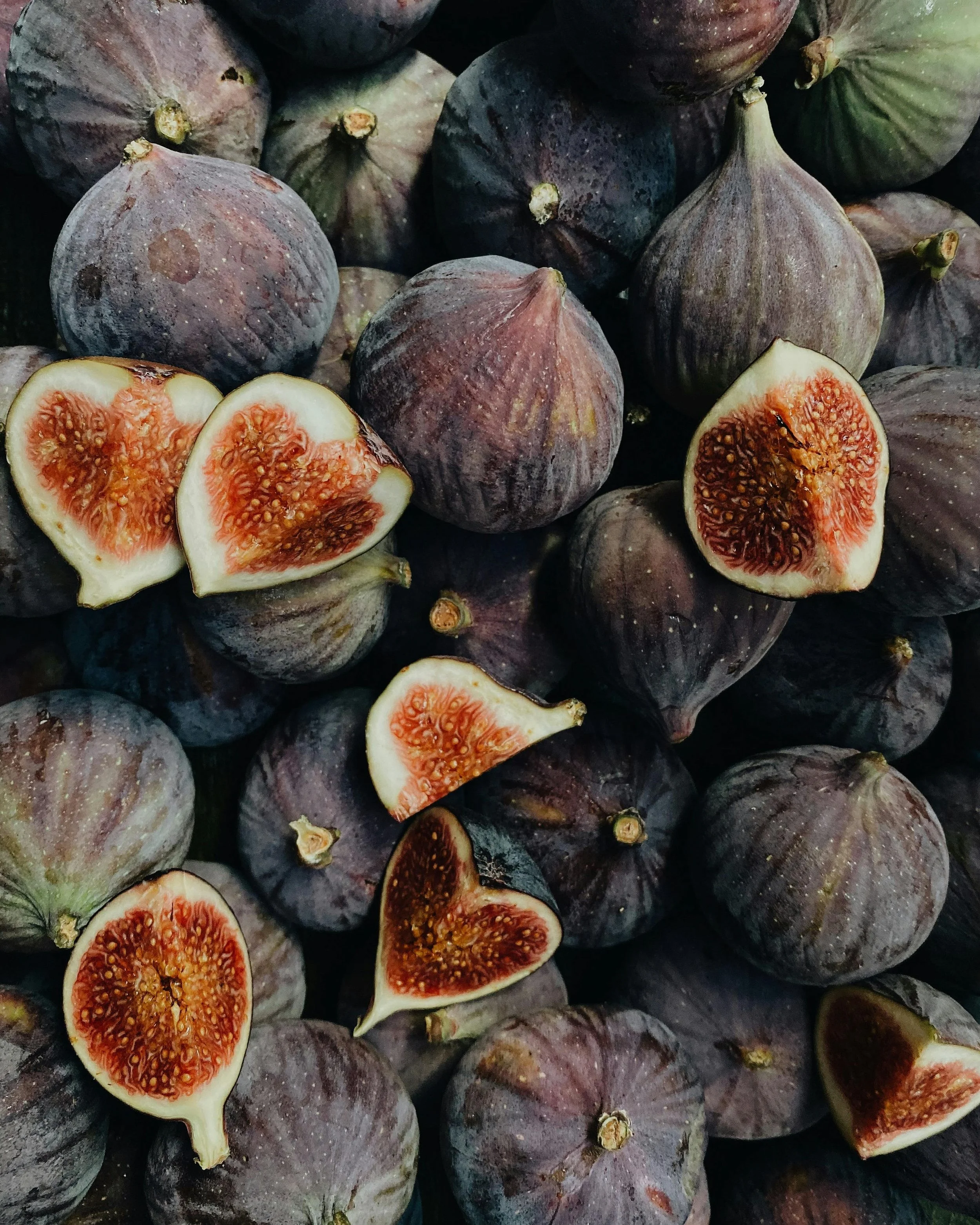 Figs, some whole and some cut open, showing the red interior with numerous tiny seeds.