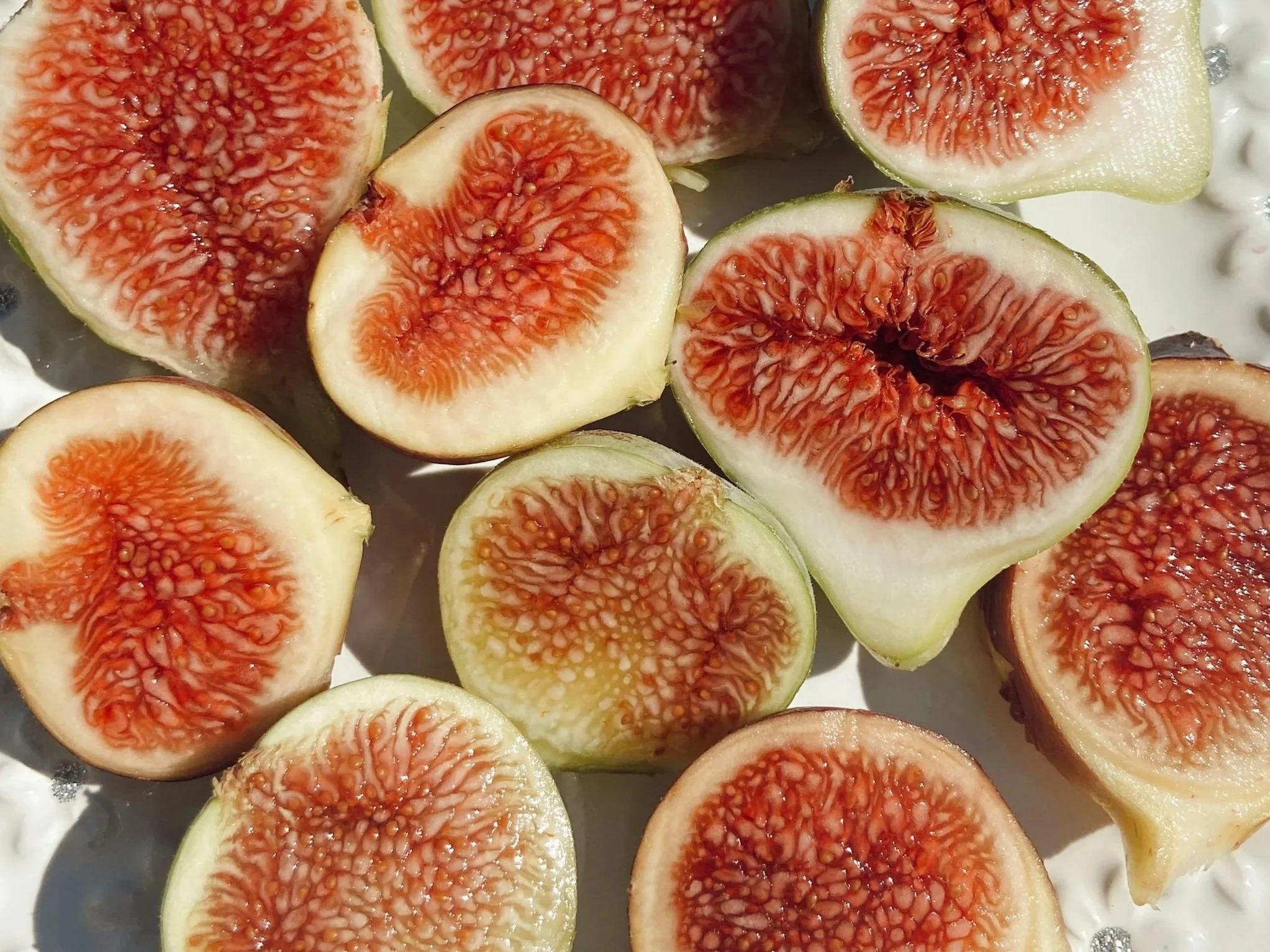 Halved fresh figs with pinkish-red interiors and greenish outer skin, arranged on a white surface.